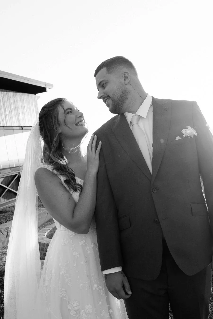 bride Chiarra stand behind groom Ben hold his shoulder while they look at each other