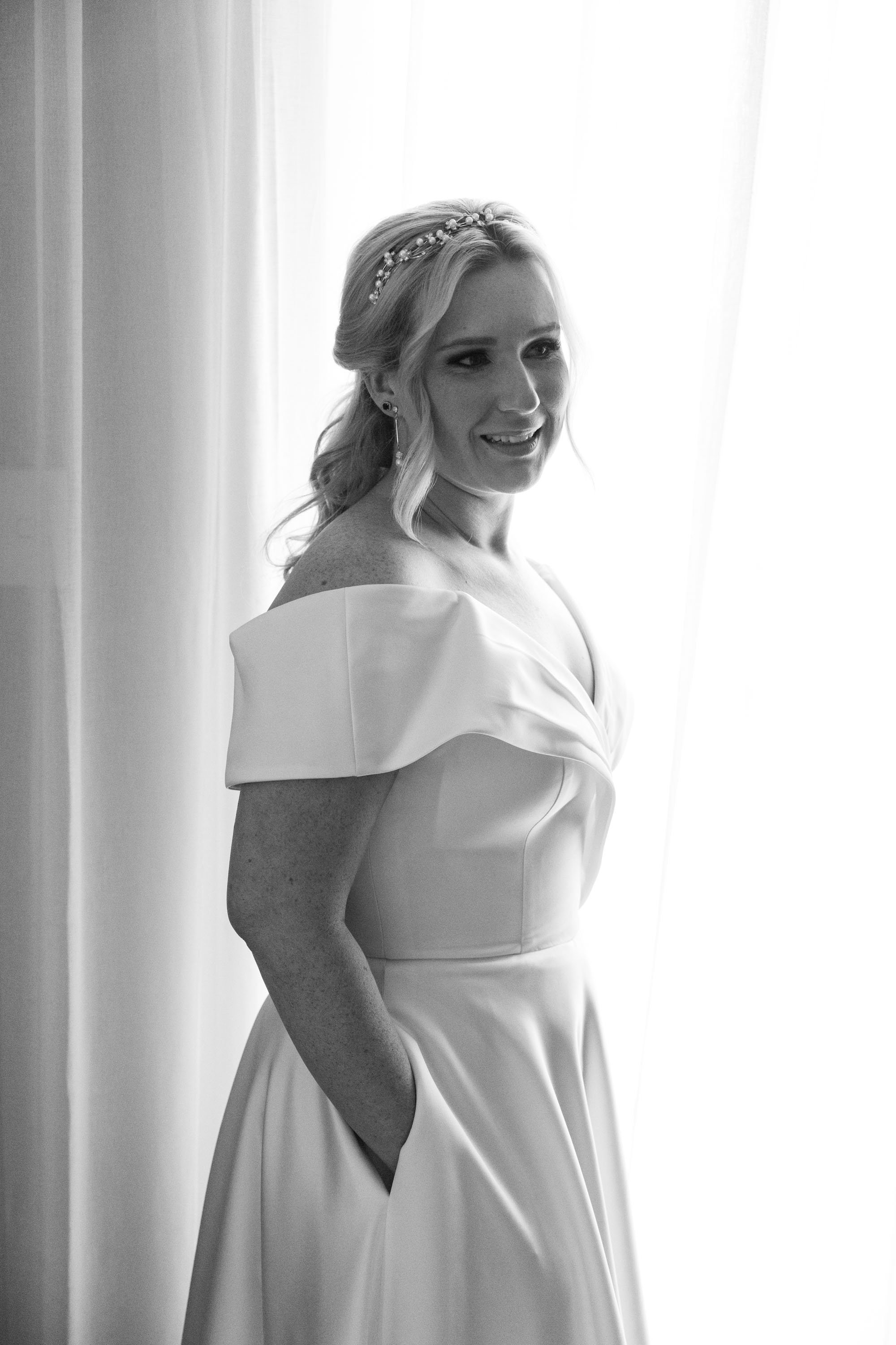 Bride Kyra with her hands inside her dress pockets, looking away thoughtfully, capturing a relaxed and contemplative moment
