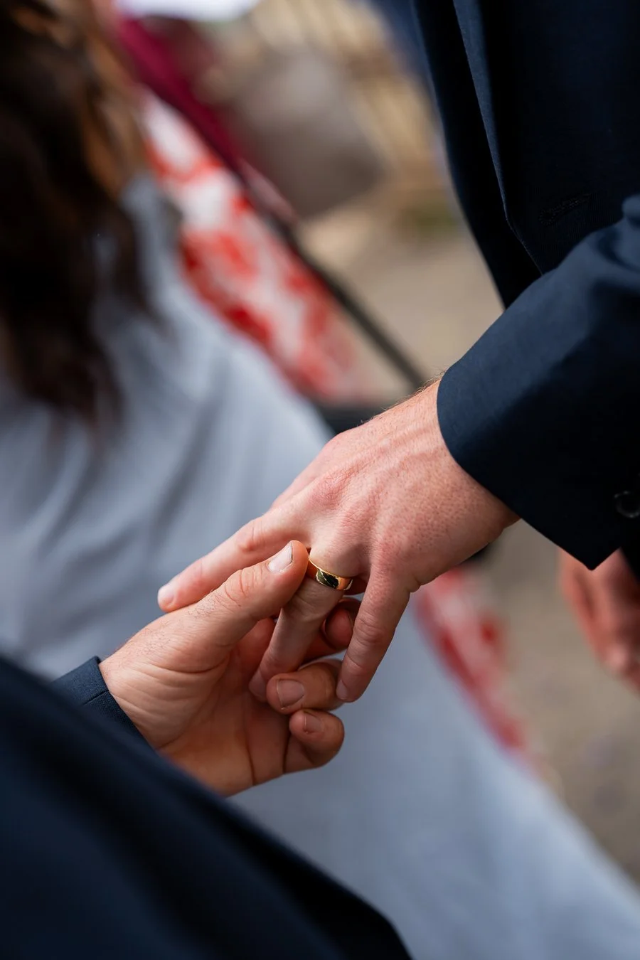 A hand gently holds the groom’s wedding ring