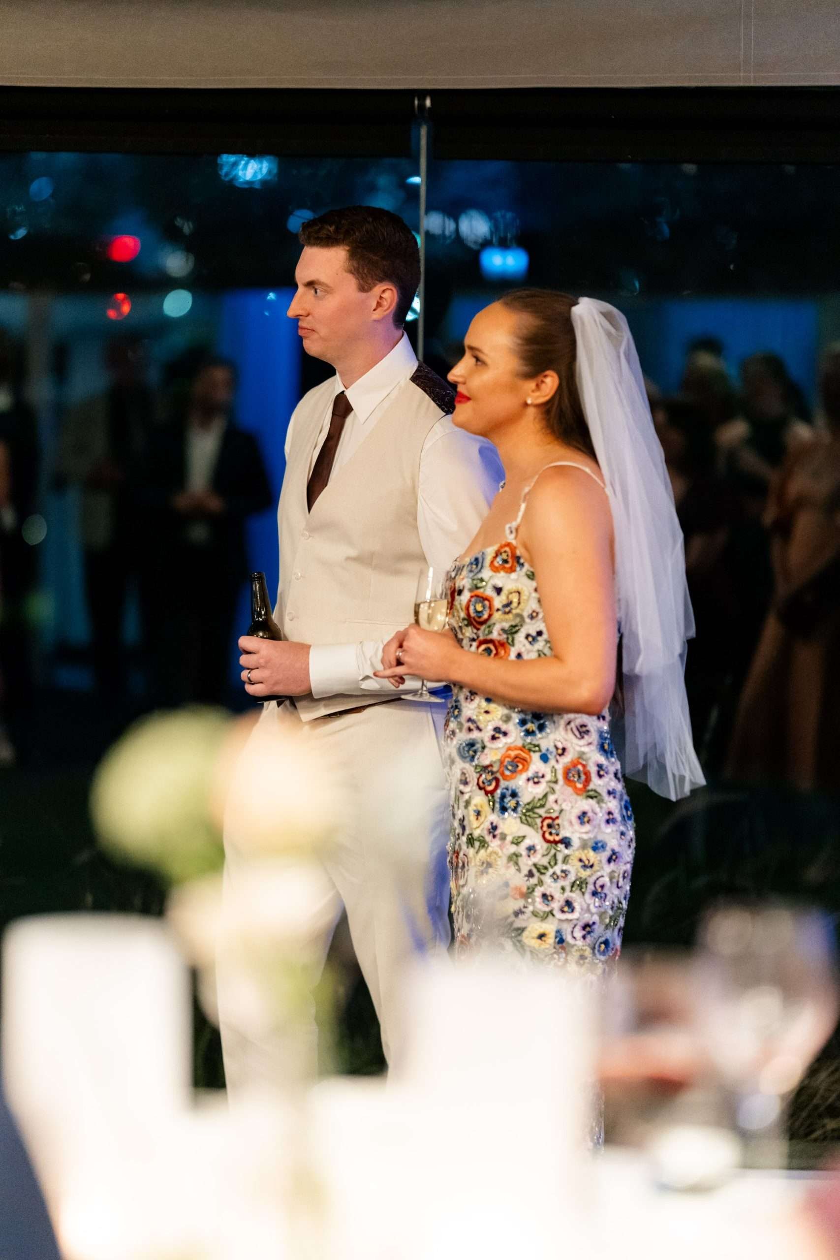 bride Charlotte and groom Jack stand together look at the speaker