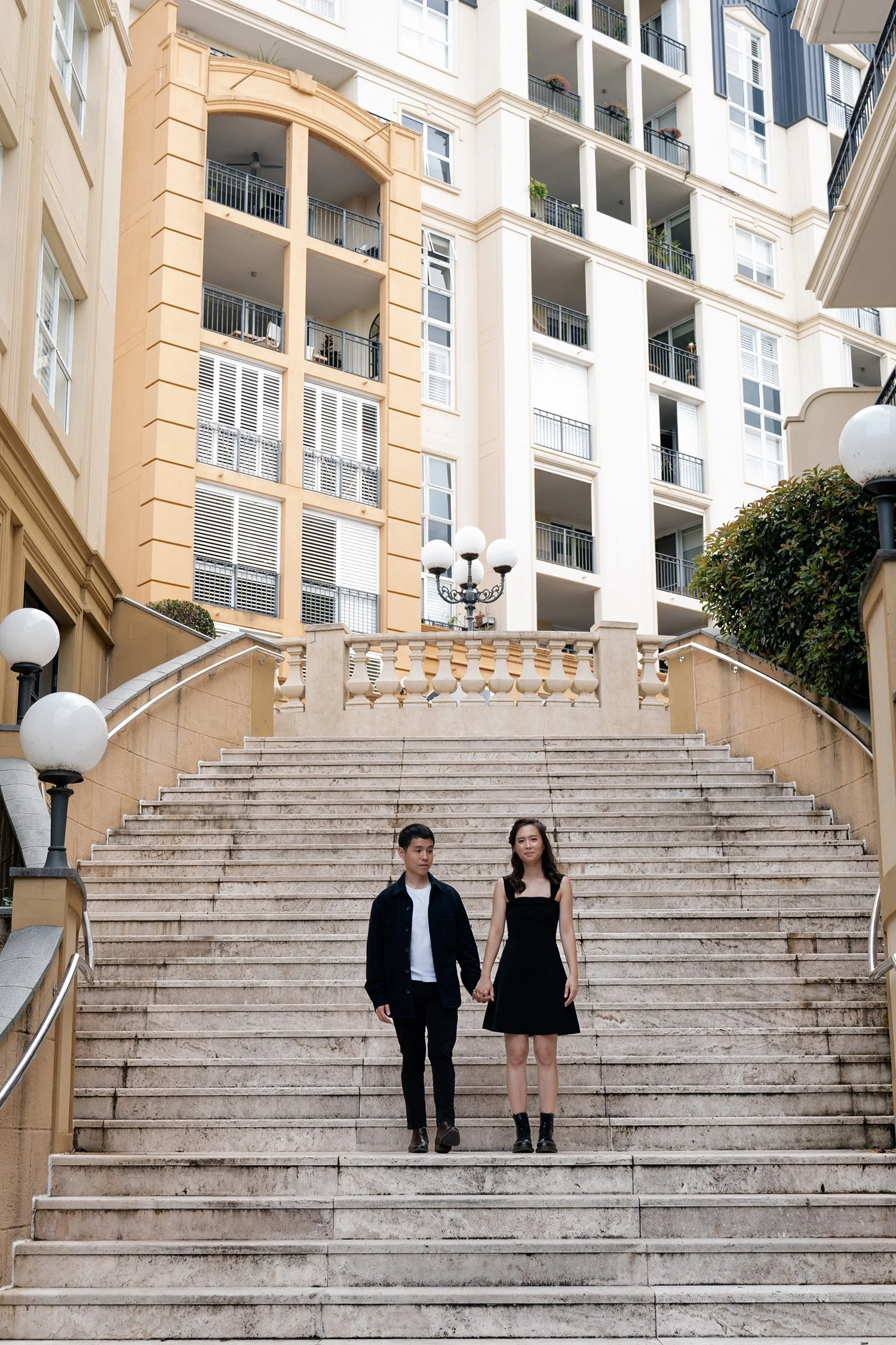 Paul and Krystel holding hands and stand on the stairs in in Emerald Lakes Village, Brisbane engagement photography