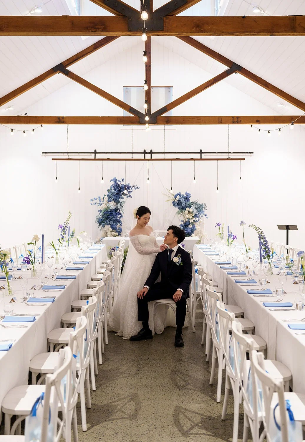 Michael sitting in the middle of their reception and Lisa stand next to him with two hands on his shoulder