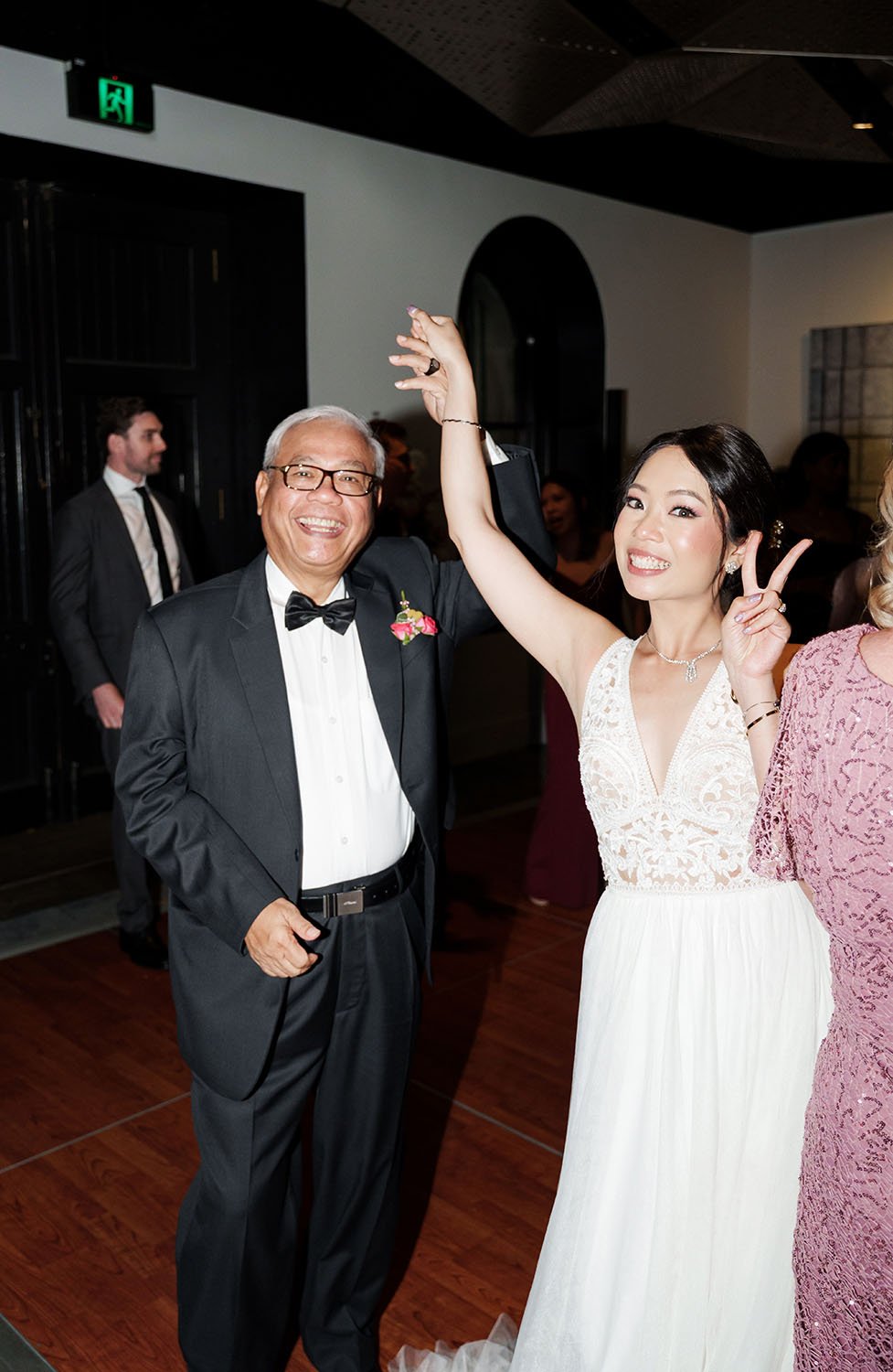 bride Nori making a victory hand gesture in front of the camera, the other hands holding her father's hands and raising up
