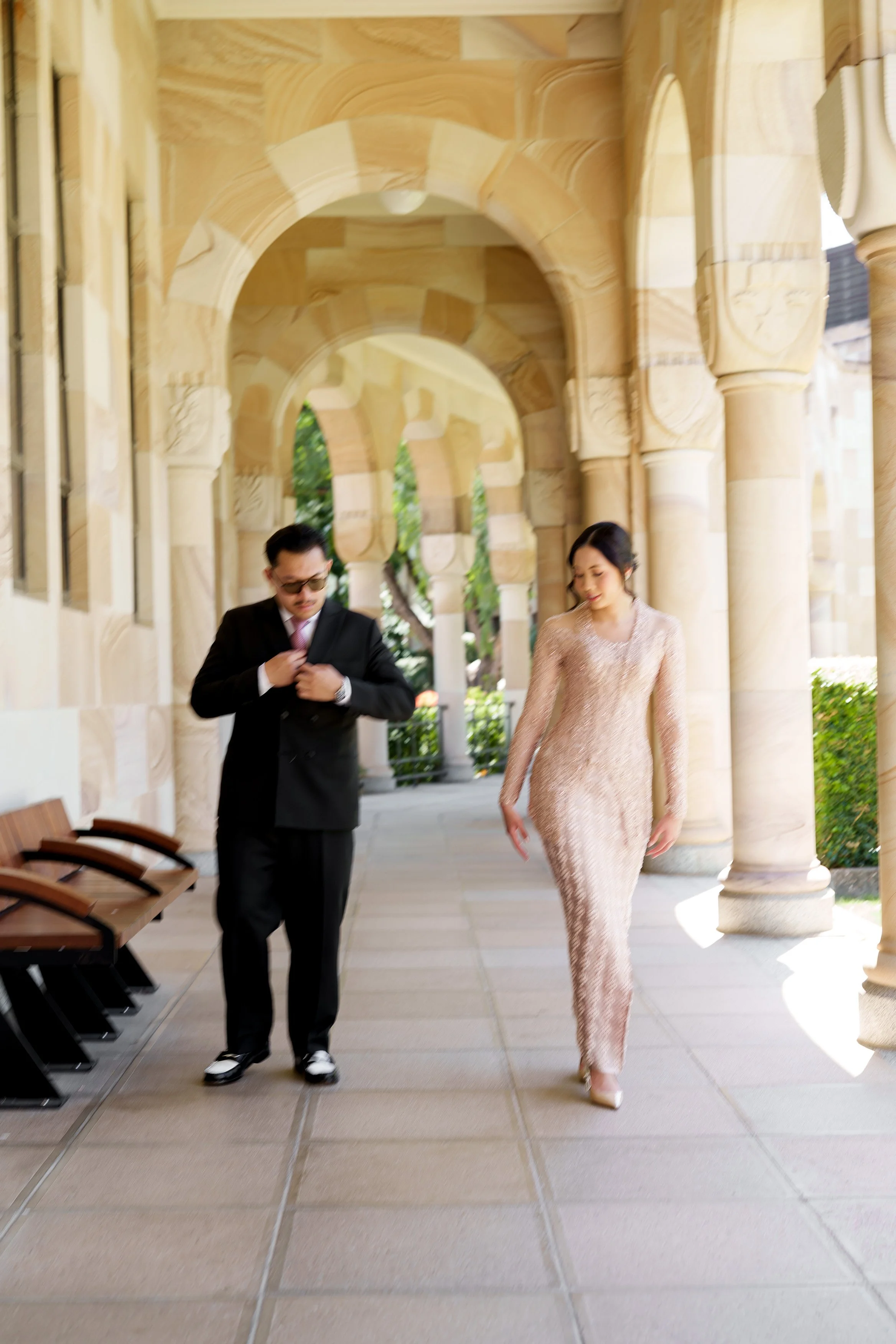 Bella and Aka walking in UQ Great Hall, Aka touching his pocket square when walking and Bella look down
