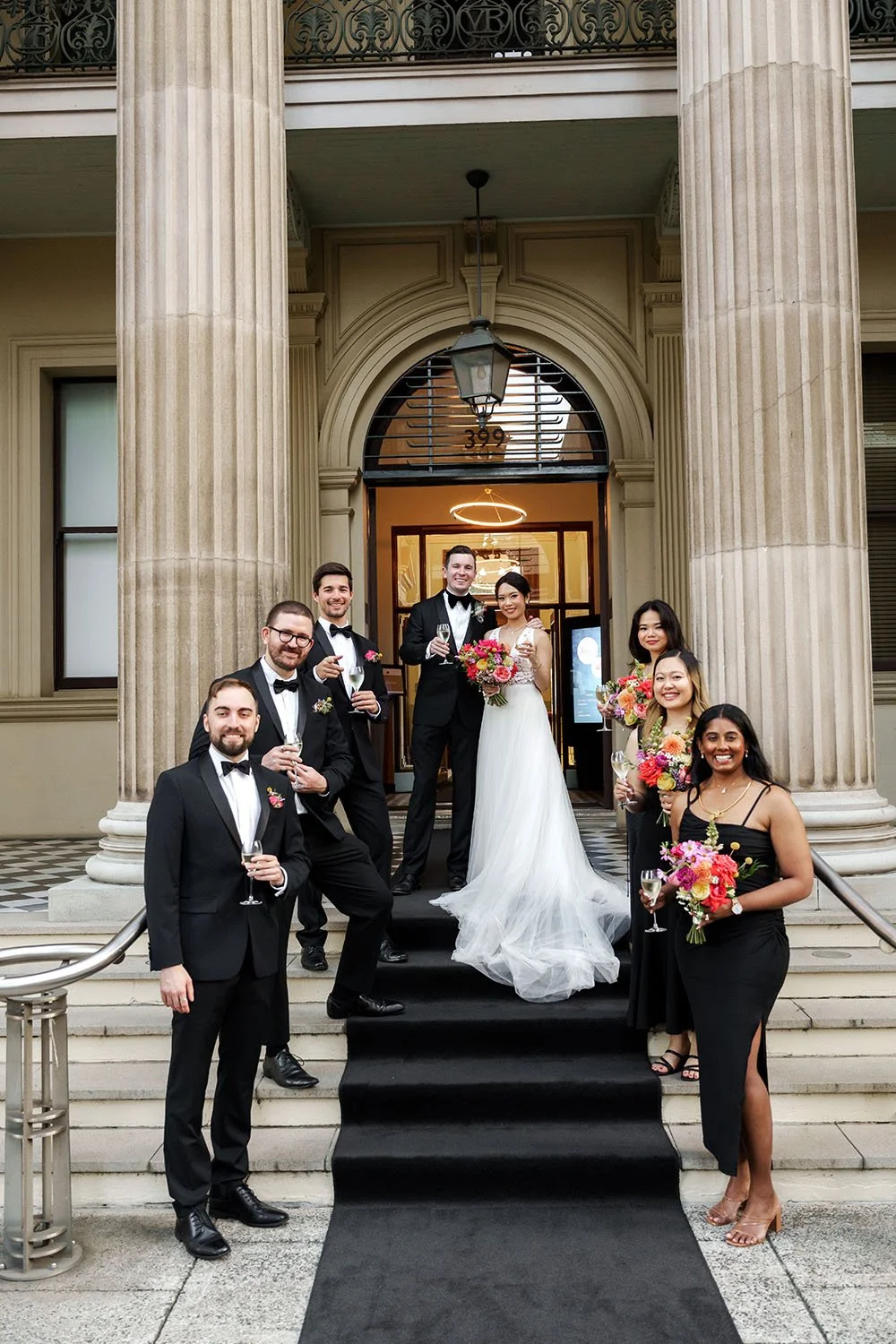 The bride and groom stand in the middle, while their bridal party stands on a different step, everyone looking at the camera