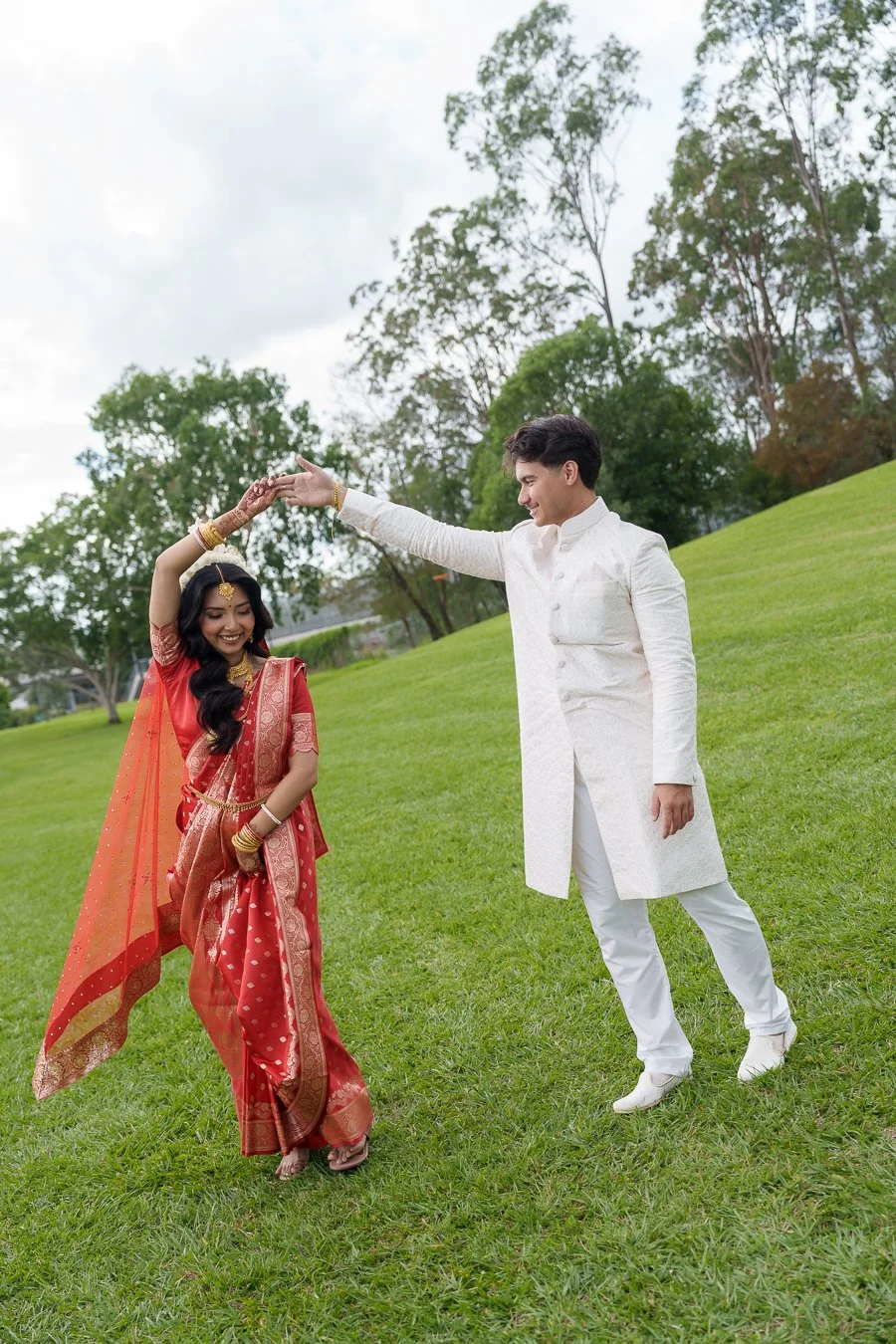 Casey spinning Amrita on grass with smell, they both in traditional Indian outfit