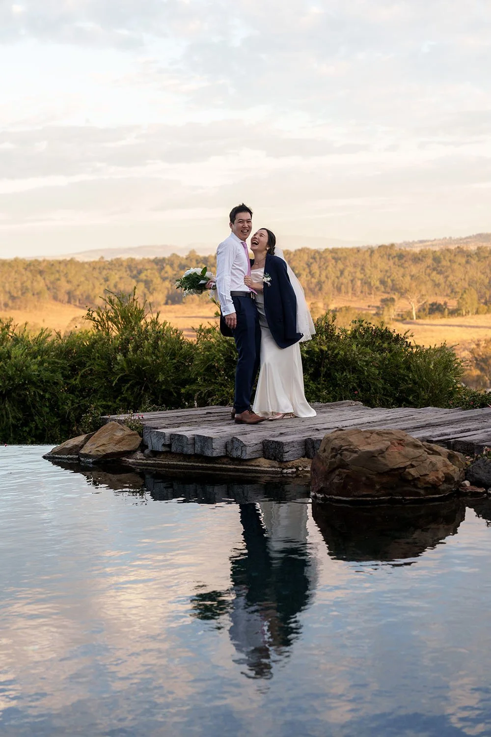 Flora holding Eric's waist and they both laughing together naturally near the water