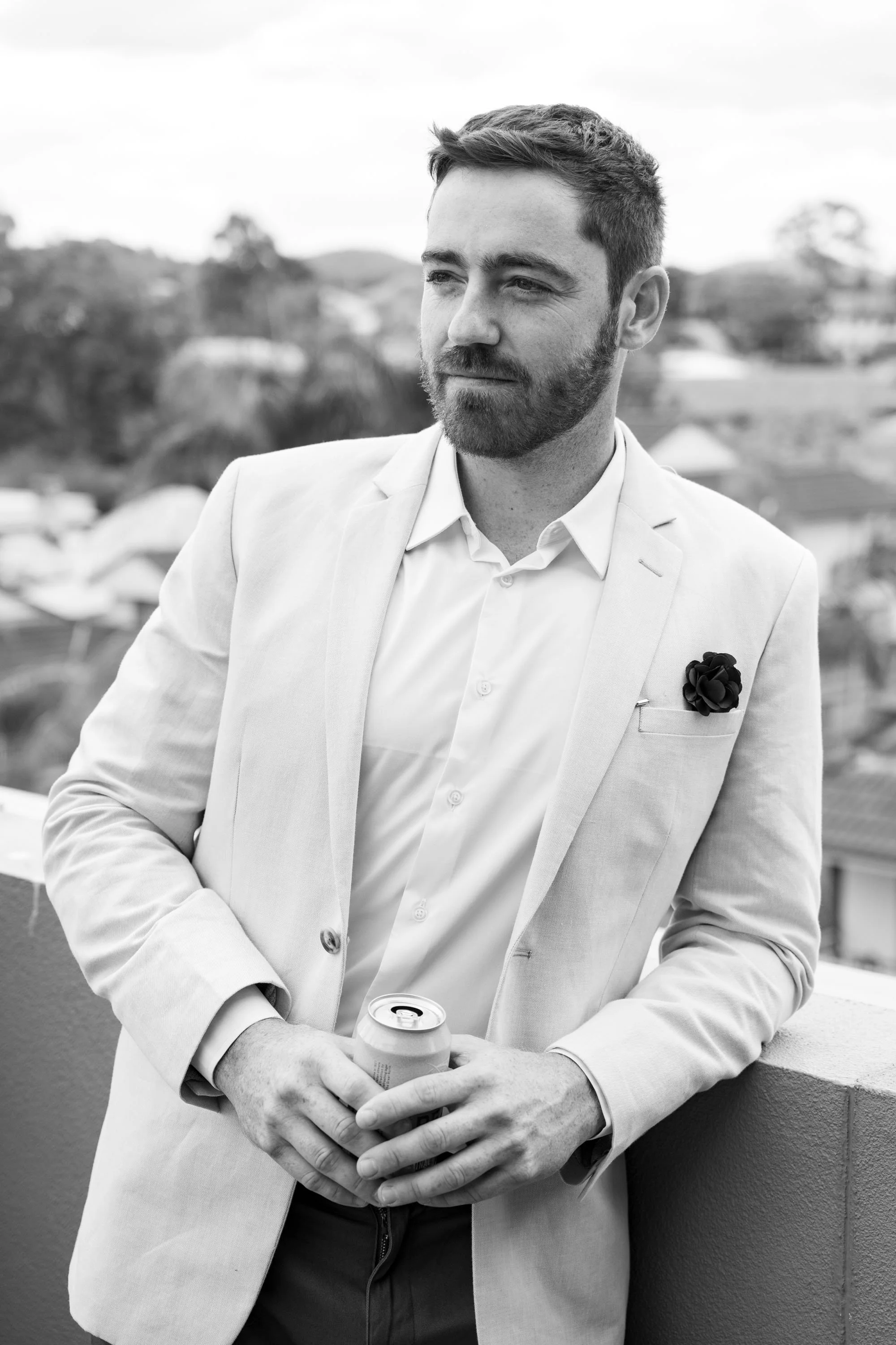 Groom Thomas holding a beer, looking away thoughtfully, capturing a relaxed moment as he enjoys the celebration of his wedding day