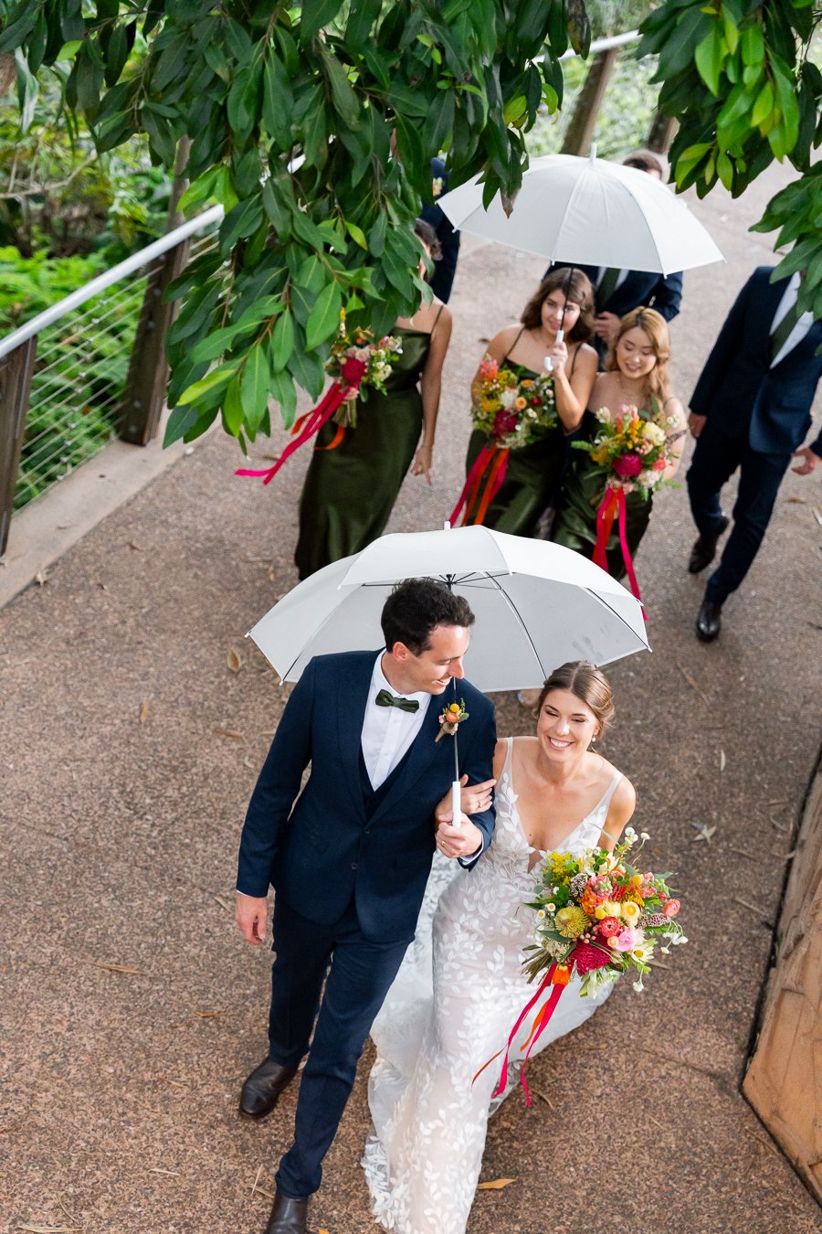 bridal party holding umbrella walking passs with all laughing
