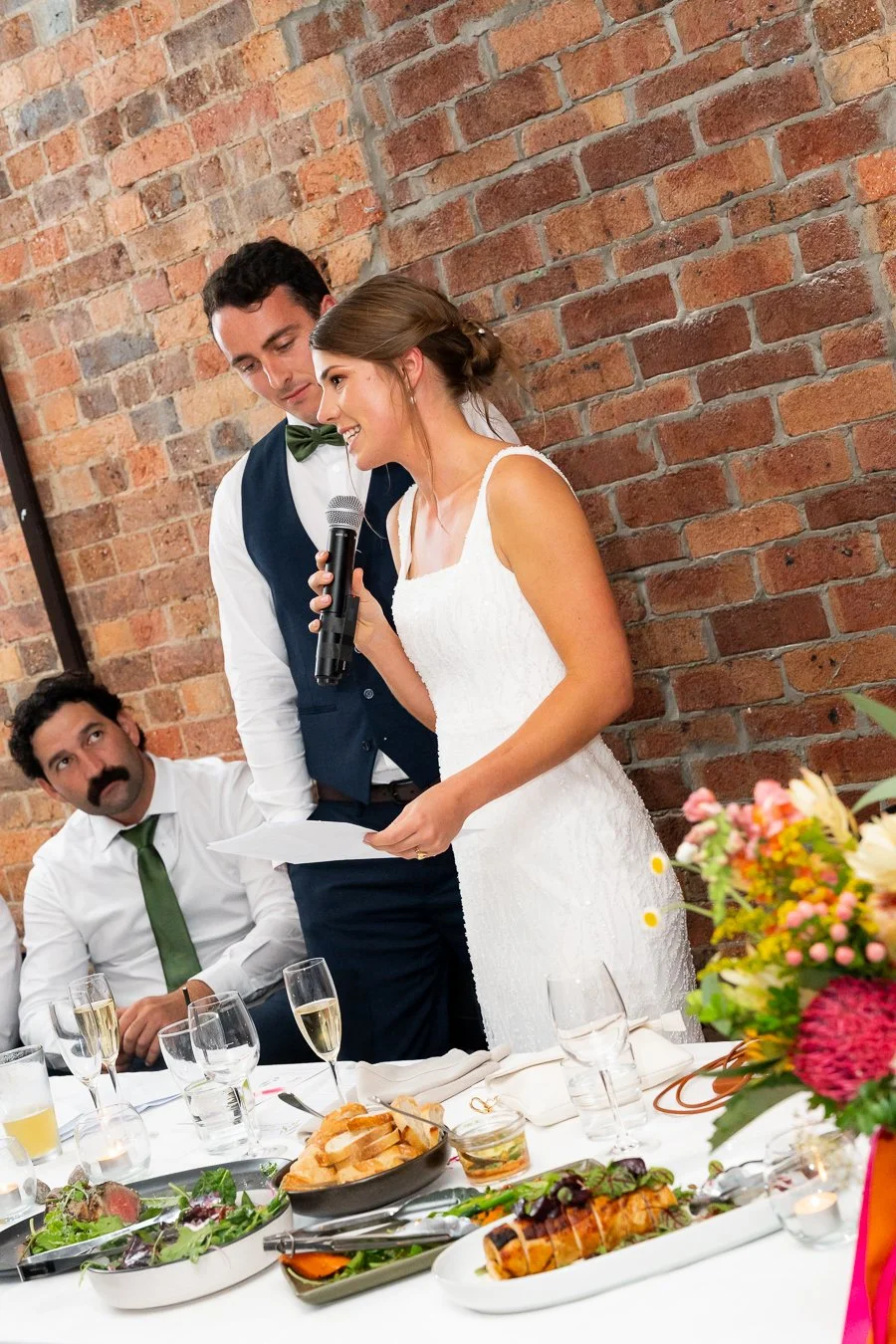 bride Sonya speak on a mic and groom Giordan stand next to her