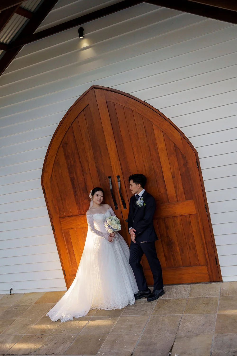 Michael and Lisa leaning on a wooden door of the white chapel, and Lisa look at the Brisbane wedding photographer Whistler Li  