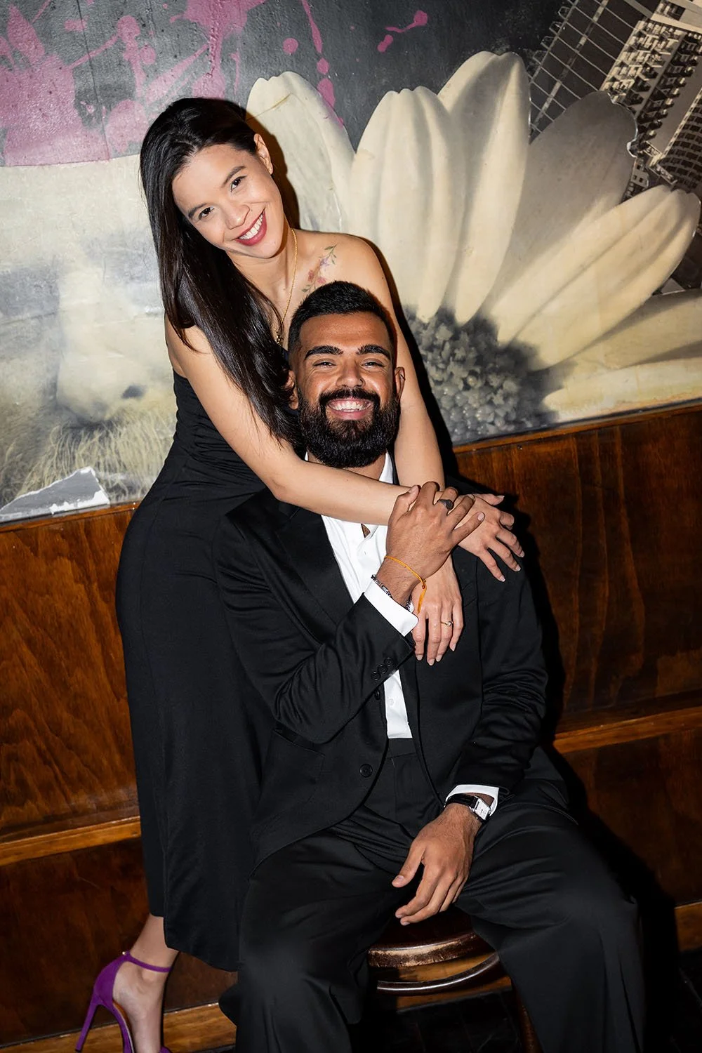 Jasmin hold jay's neck while jay sitting on a chair look at the photographer