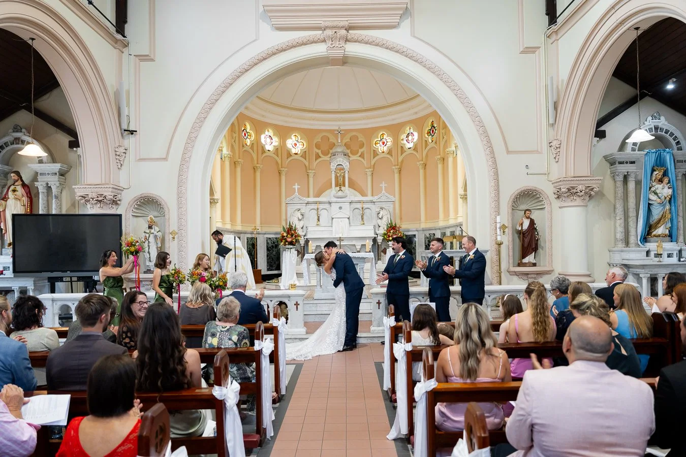 The bride and groom kiss while everyone applauds.