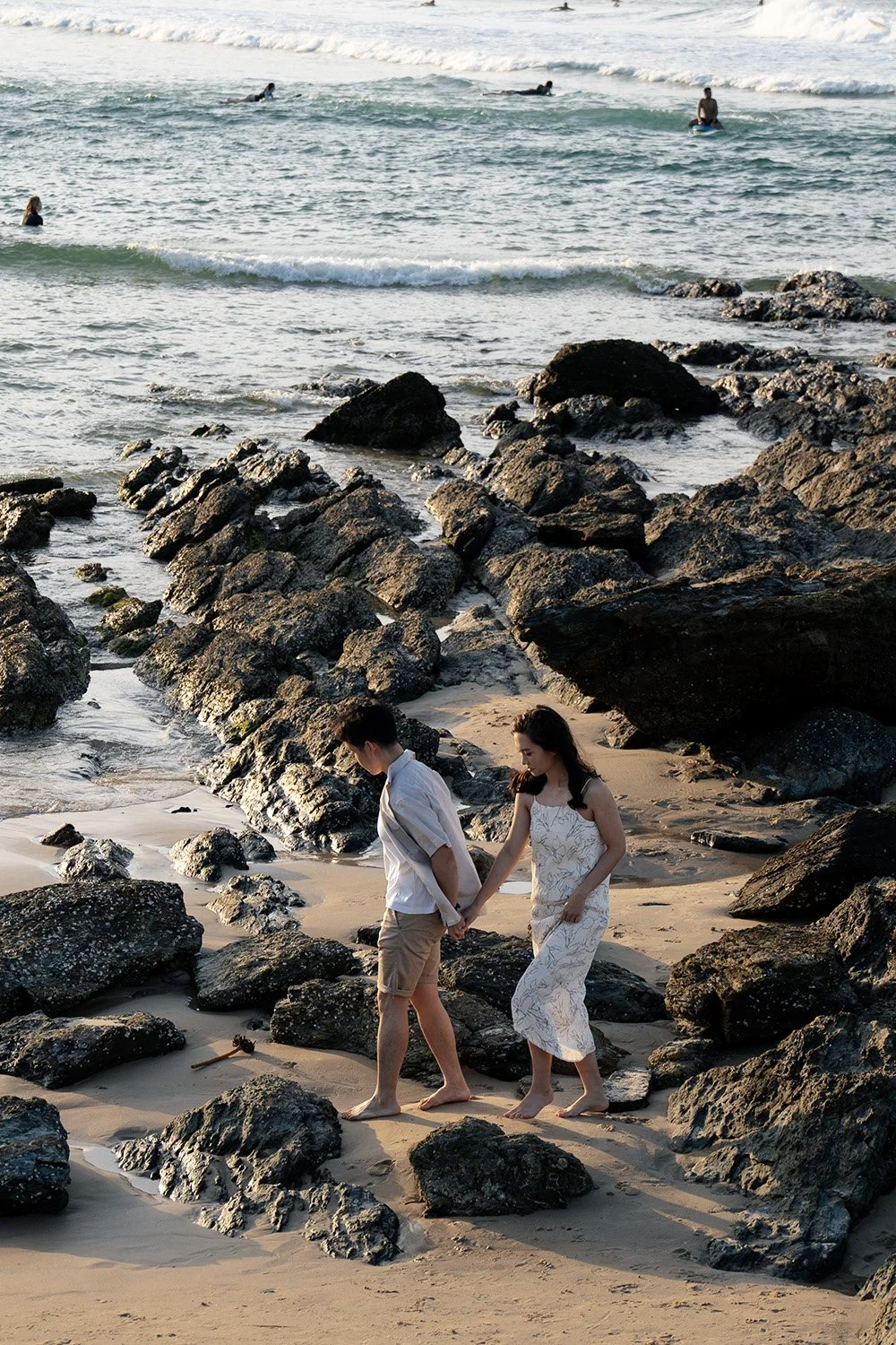 Paul and Krystel holding hands walking on the rocky surface towards the Gold Coast city view