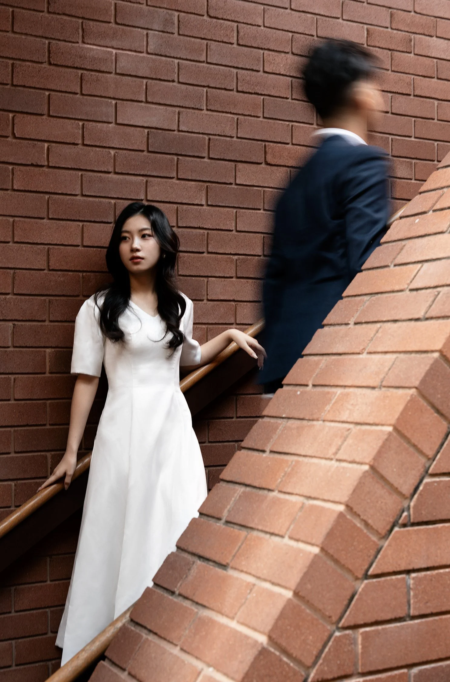 bride leaning back the brick wall and groom walking up to the stairs