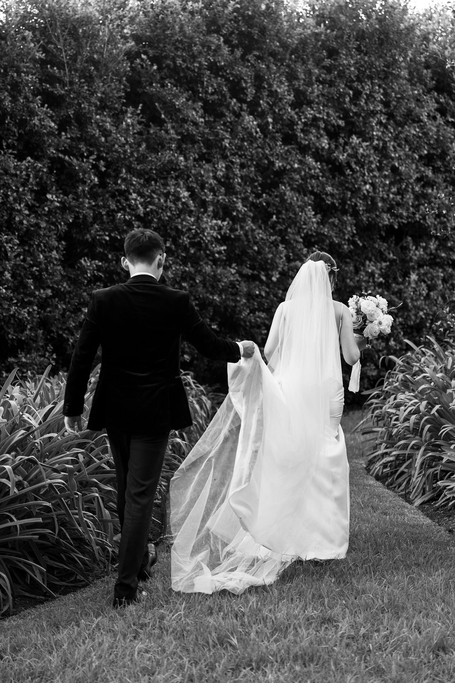 groom Brus holding a tile of bride's dress and they walking away from the camera
