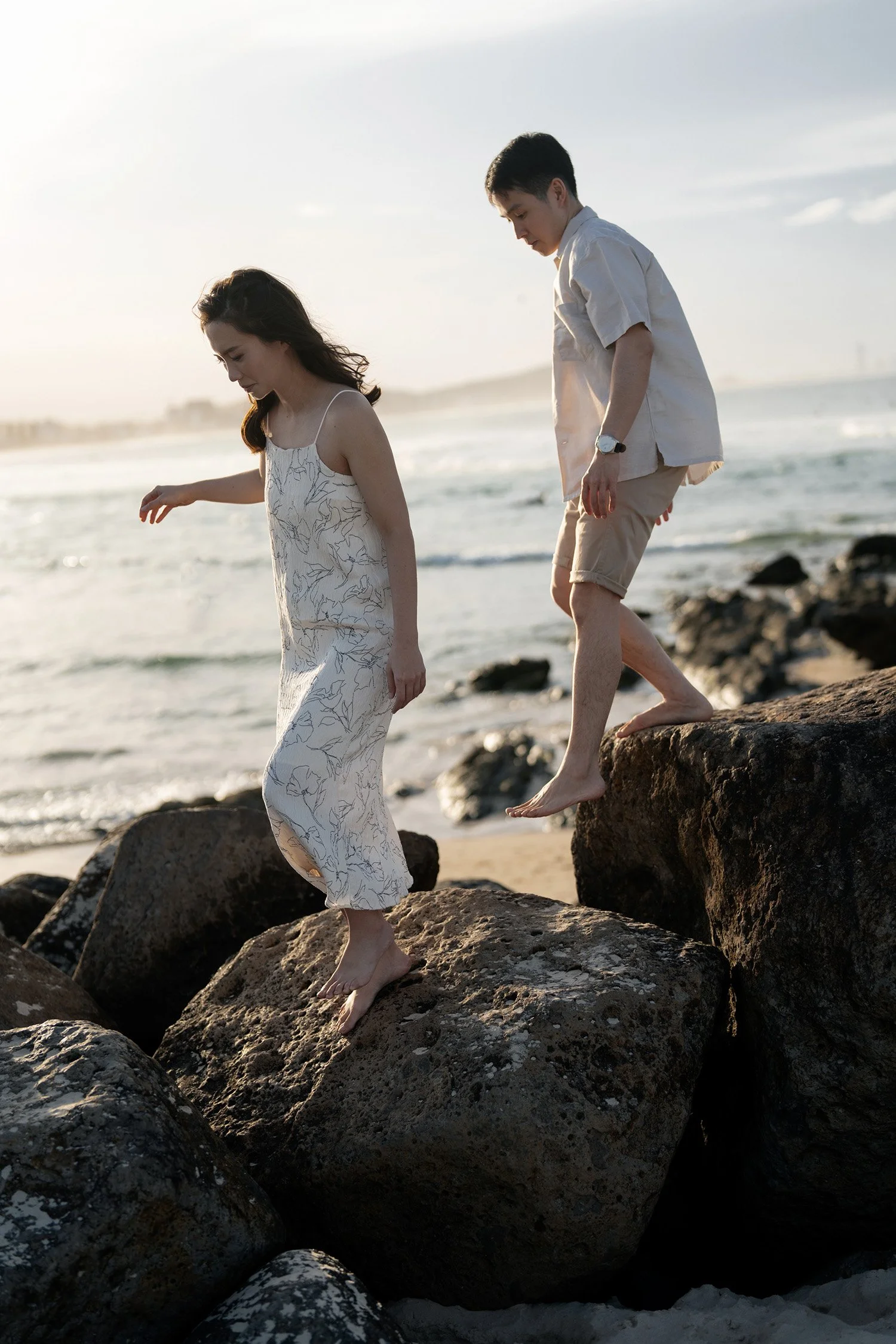 Paul and Krystel walking hand in hand on Currumbin Rock, surrounded by the natural beauty of the landscape. The couple's relaxed and joyful moment is captured against the stunning backdrop of the rugged rock formations and coastal views.
