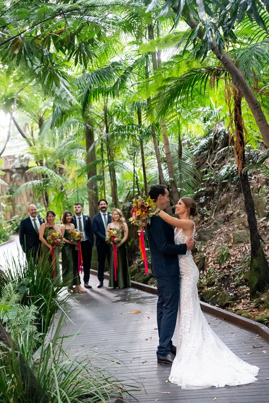 The bride and groom hold each other close, as the bridal party watch from a few steps behind