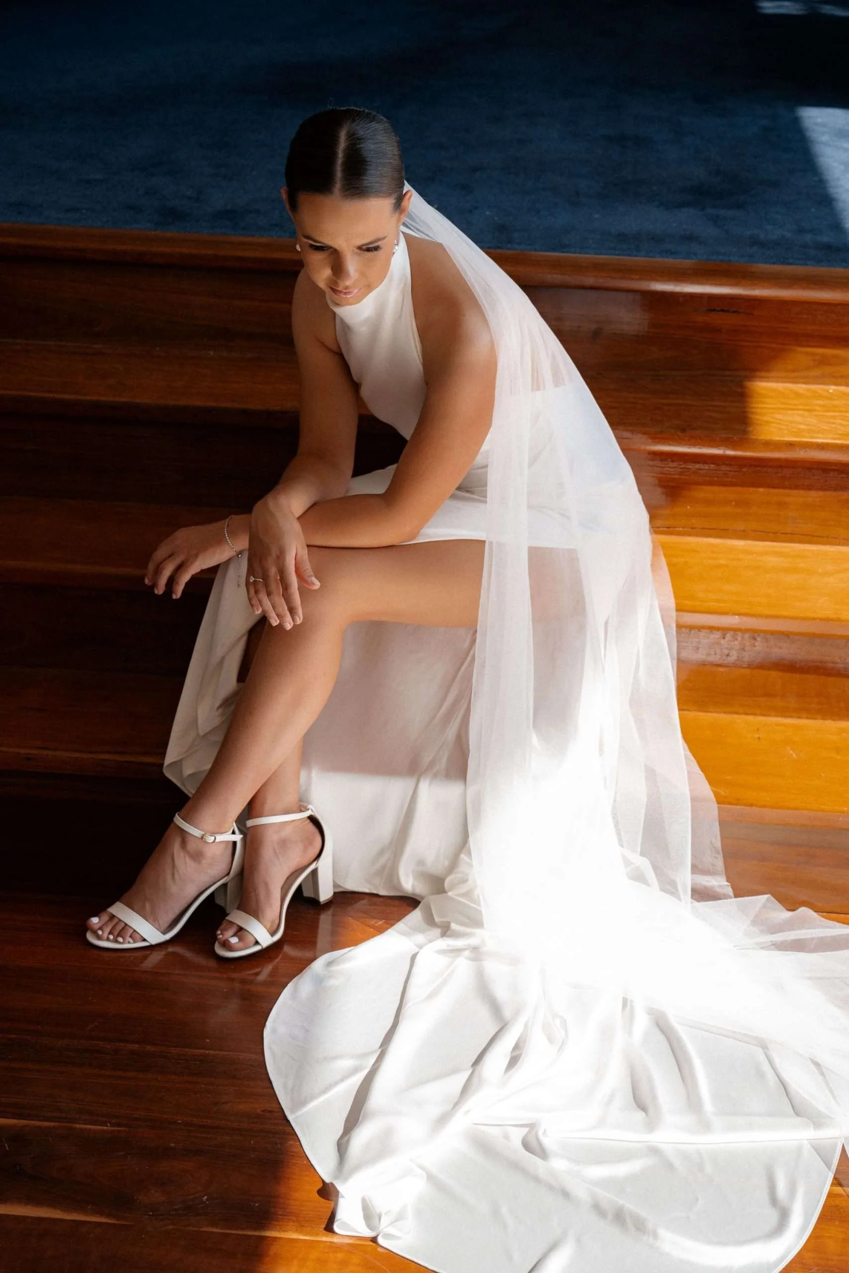 Sam in her wedding dress sitting on the stairs and look down to the flower, light behind her
