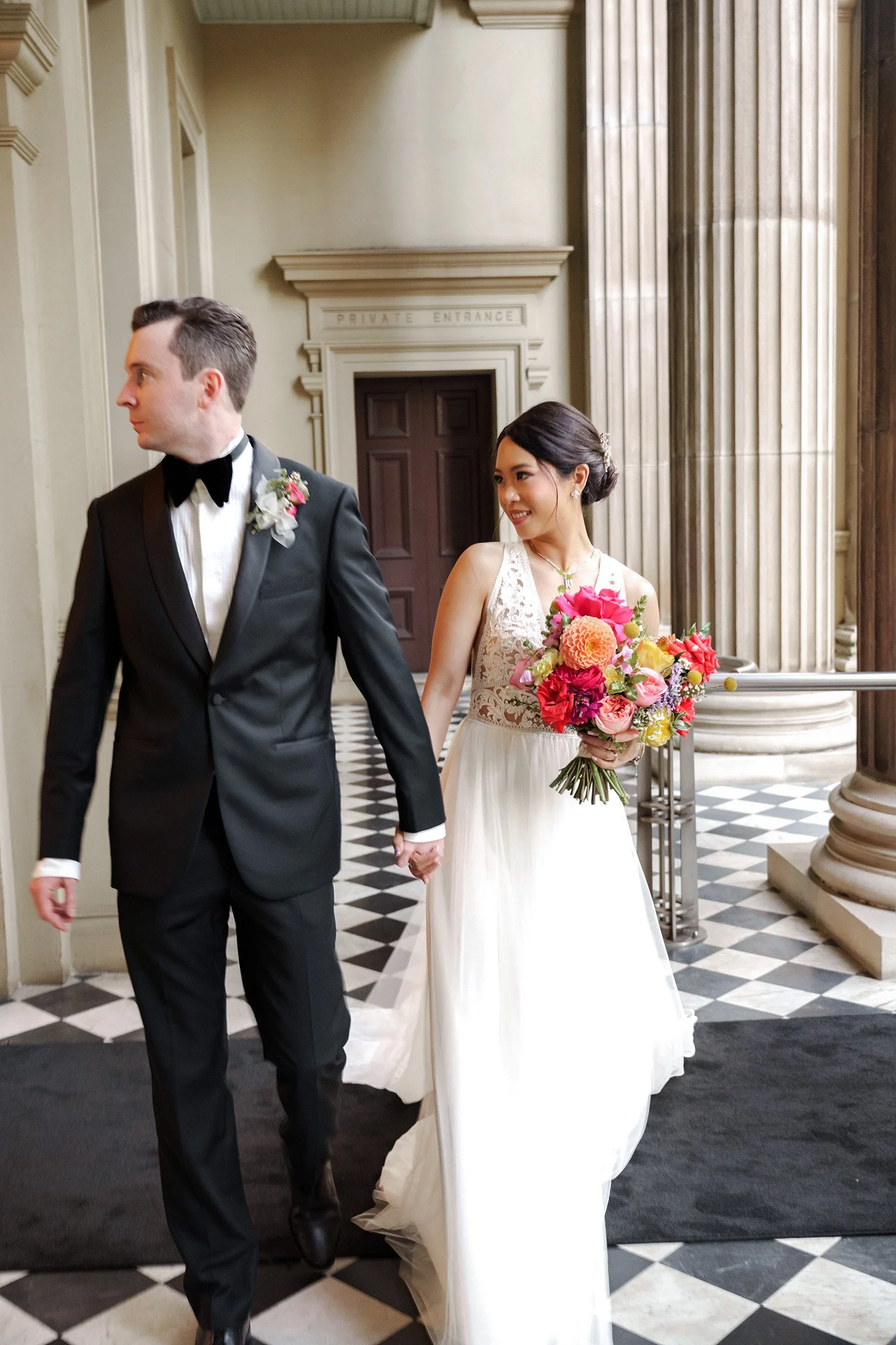 groom Cliffe holding bride Nori's hand walking towards to the Brisbane wedding photographer Whistler Li, and groom look inside the room with yellow light hit on her face while bride look hime