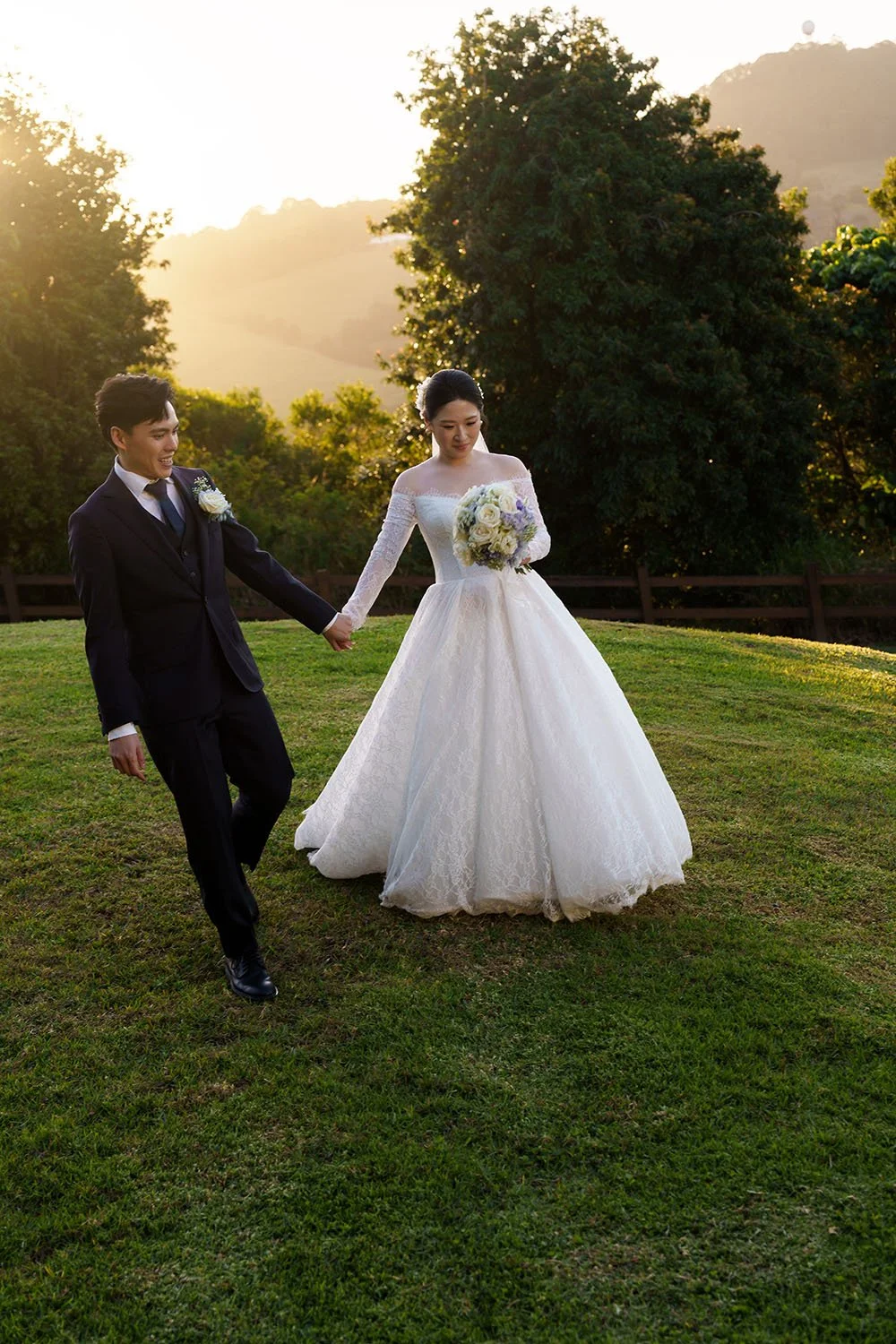 Michael holding Lisa walking on the grass with sun behind them in Summergrove estate