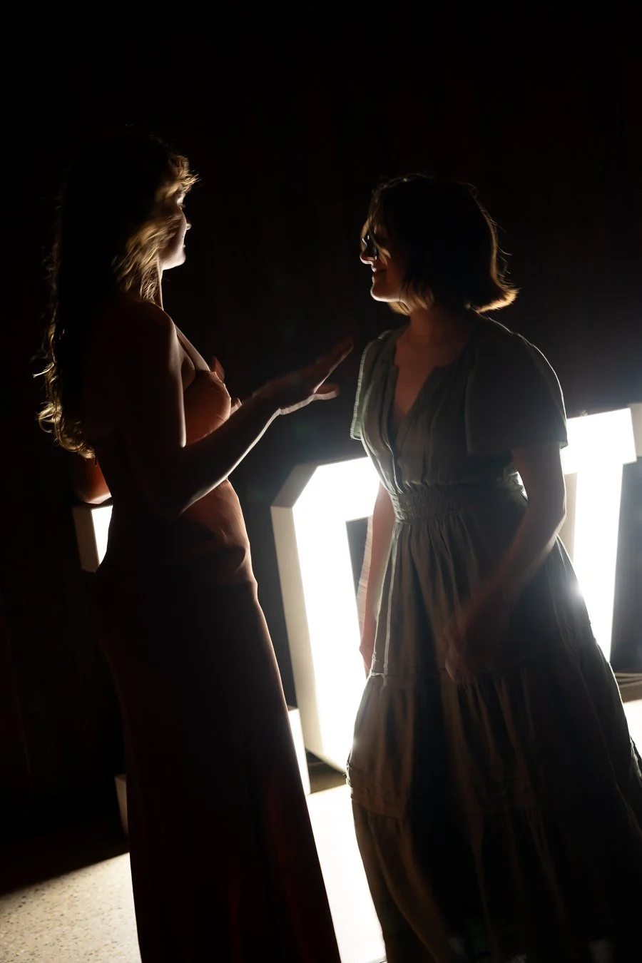 two females facing each other dancing in front of love led lights