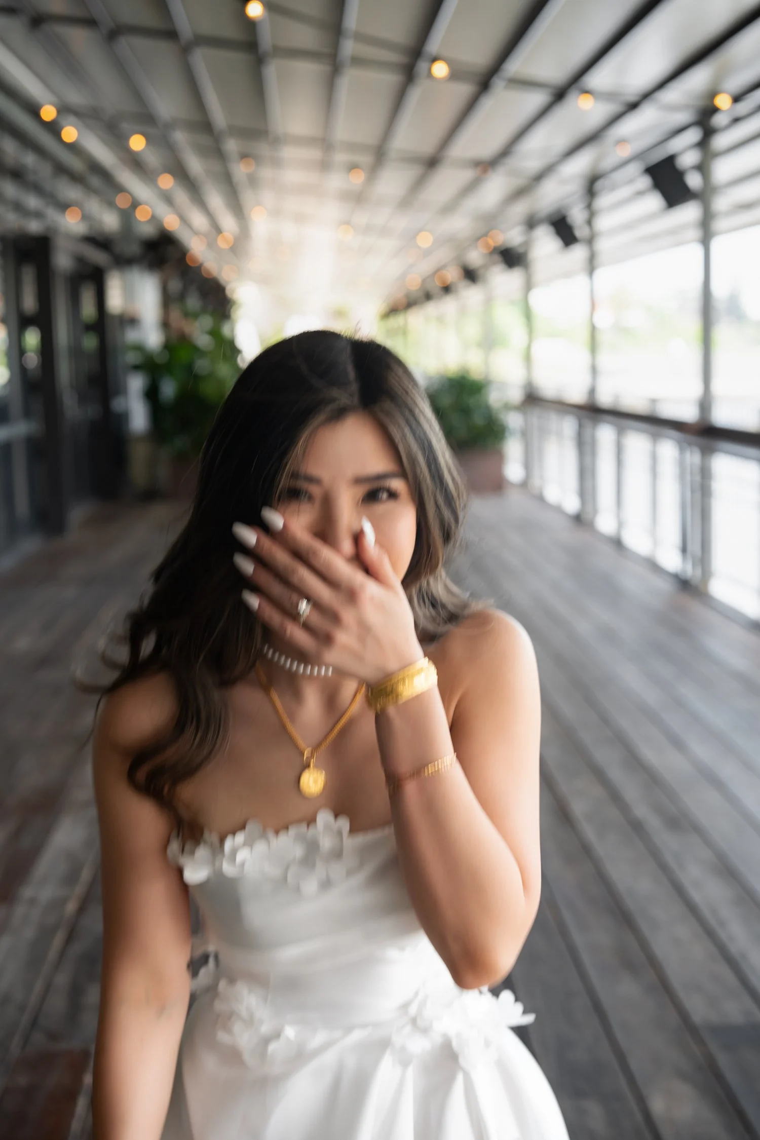 Bride Tiffy smiling at the camera with a playful expression, gently covering her mouth with her hand. Her joyful and slightly shy gesture adds a charming and intimate touch to the moment, showcasing her beauty and happiness on her wedding day.