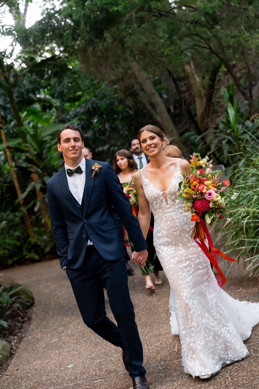 bride and groom look the Brisbane wedding photographer Whist er Li the waling, bridal party walking behind them