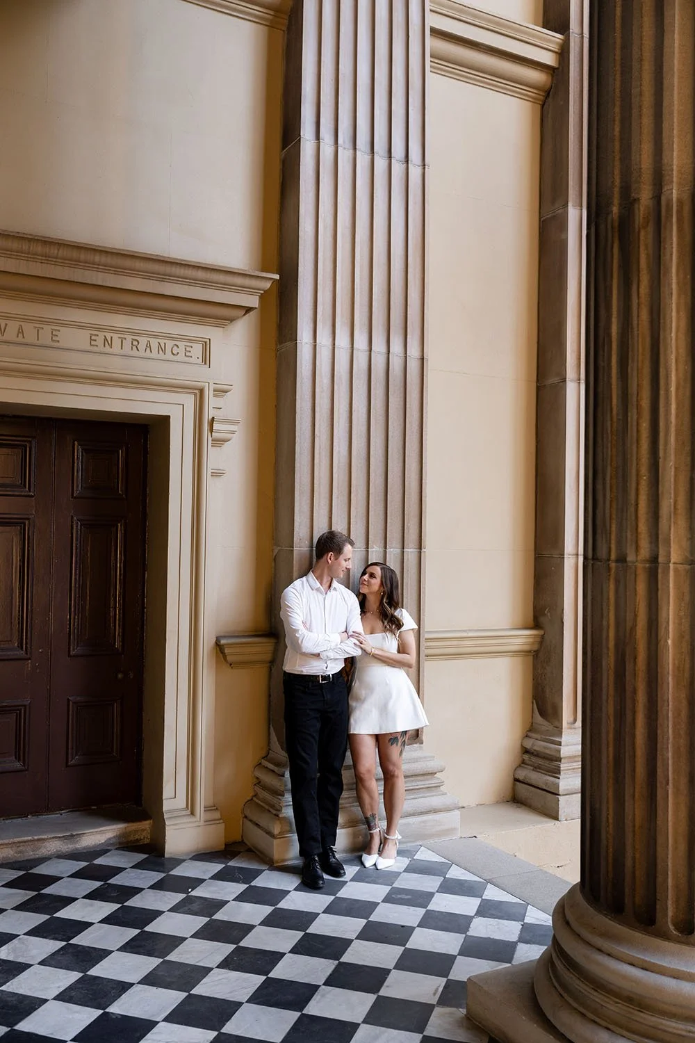 Brenna and Morgan leaning on the wall look at each other in their Brisbane engagement photo session capture by Brisbane wedding photographer Whistler