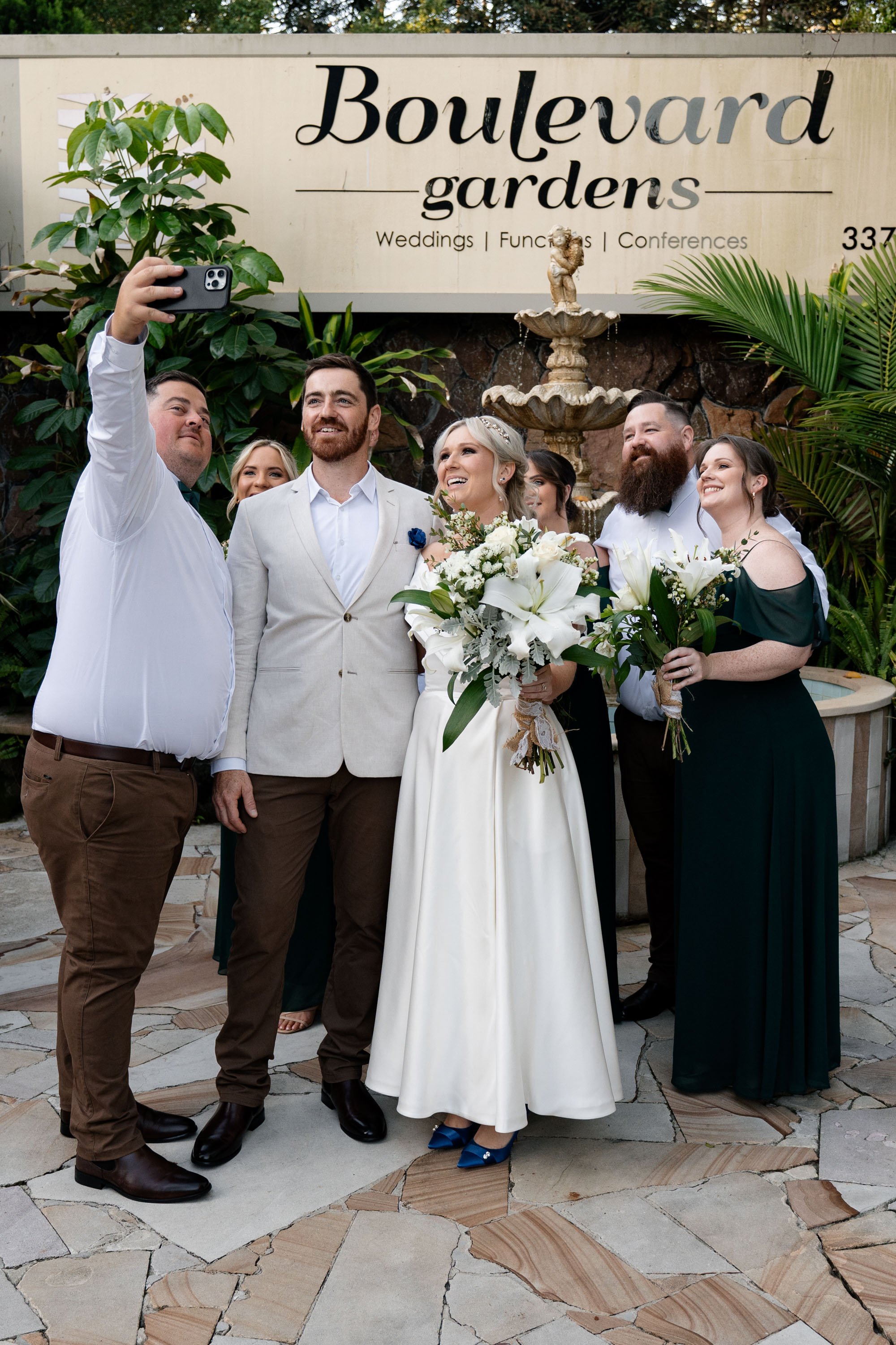 Bridal party taking a fun selfie together in front of a fountain, capturing a lighthearted and memorable moment during the wedding day