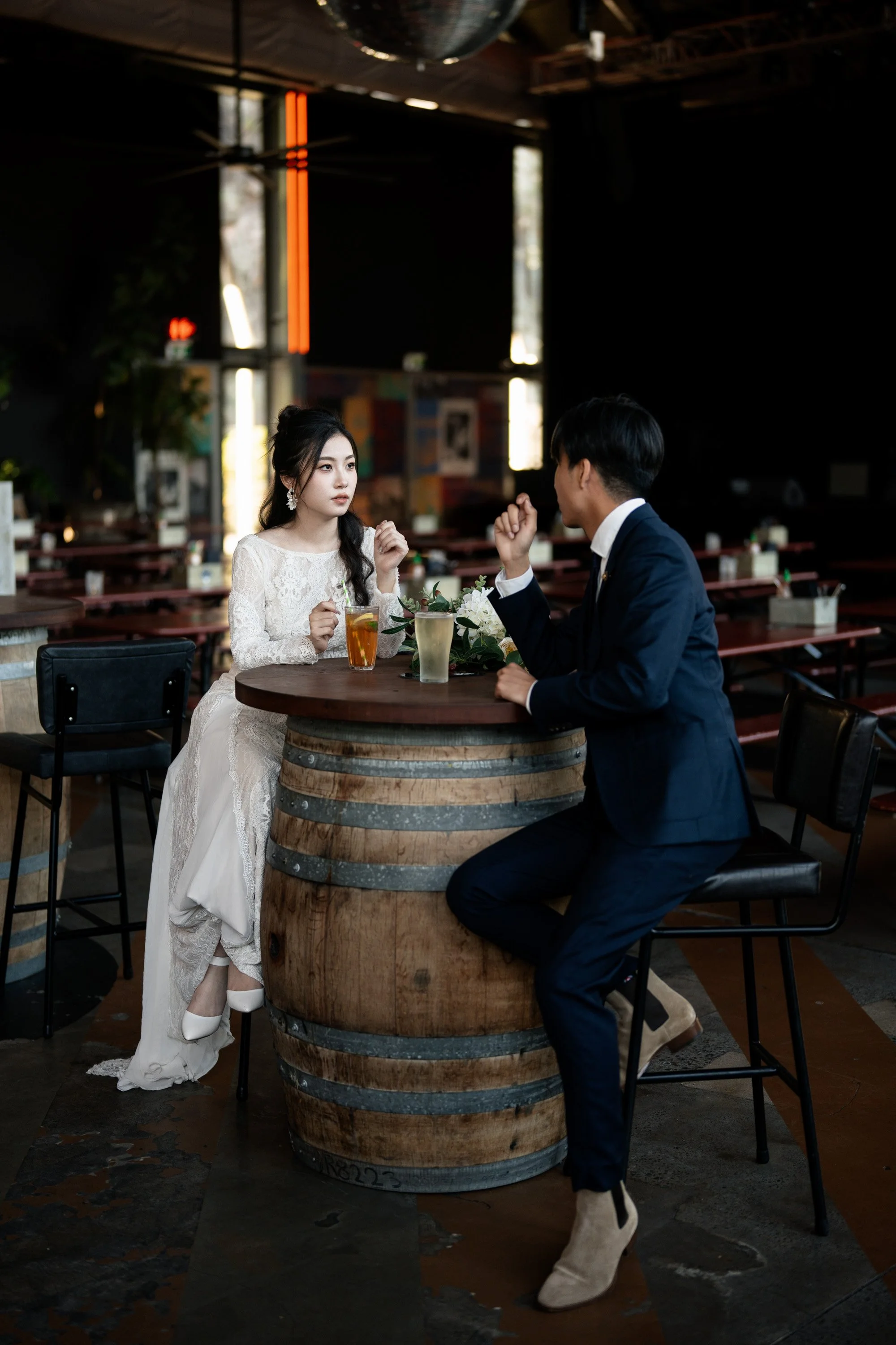 bride and groom sitting next a wine barrel with some drinks and look at each other