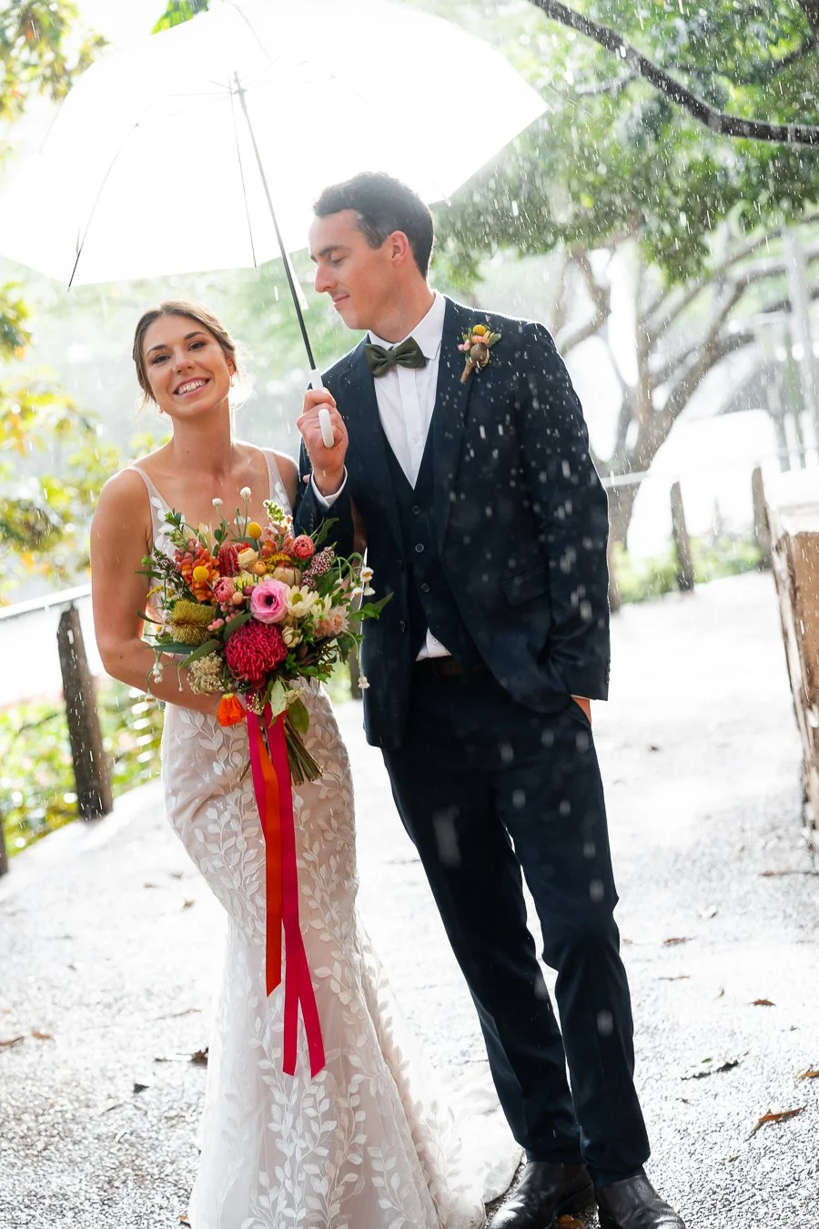 The groom is holding an umbrella, and the bride stands beside him, holding his arm and looking at Brisbane wedding photographer Whistler