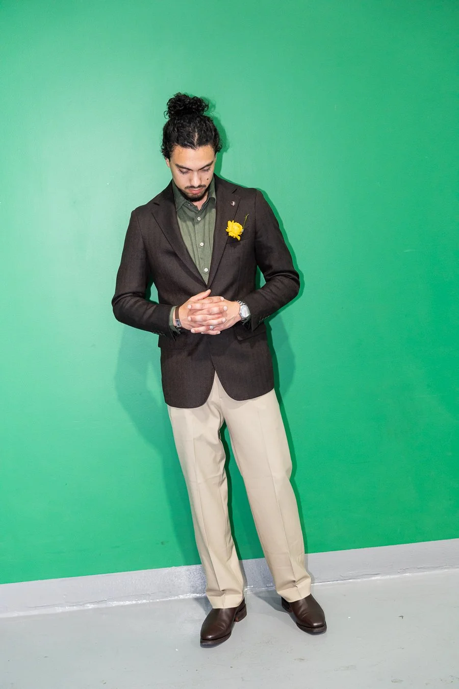 Junaid crossing his hands and look down standing infant of a green wall