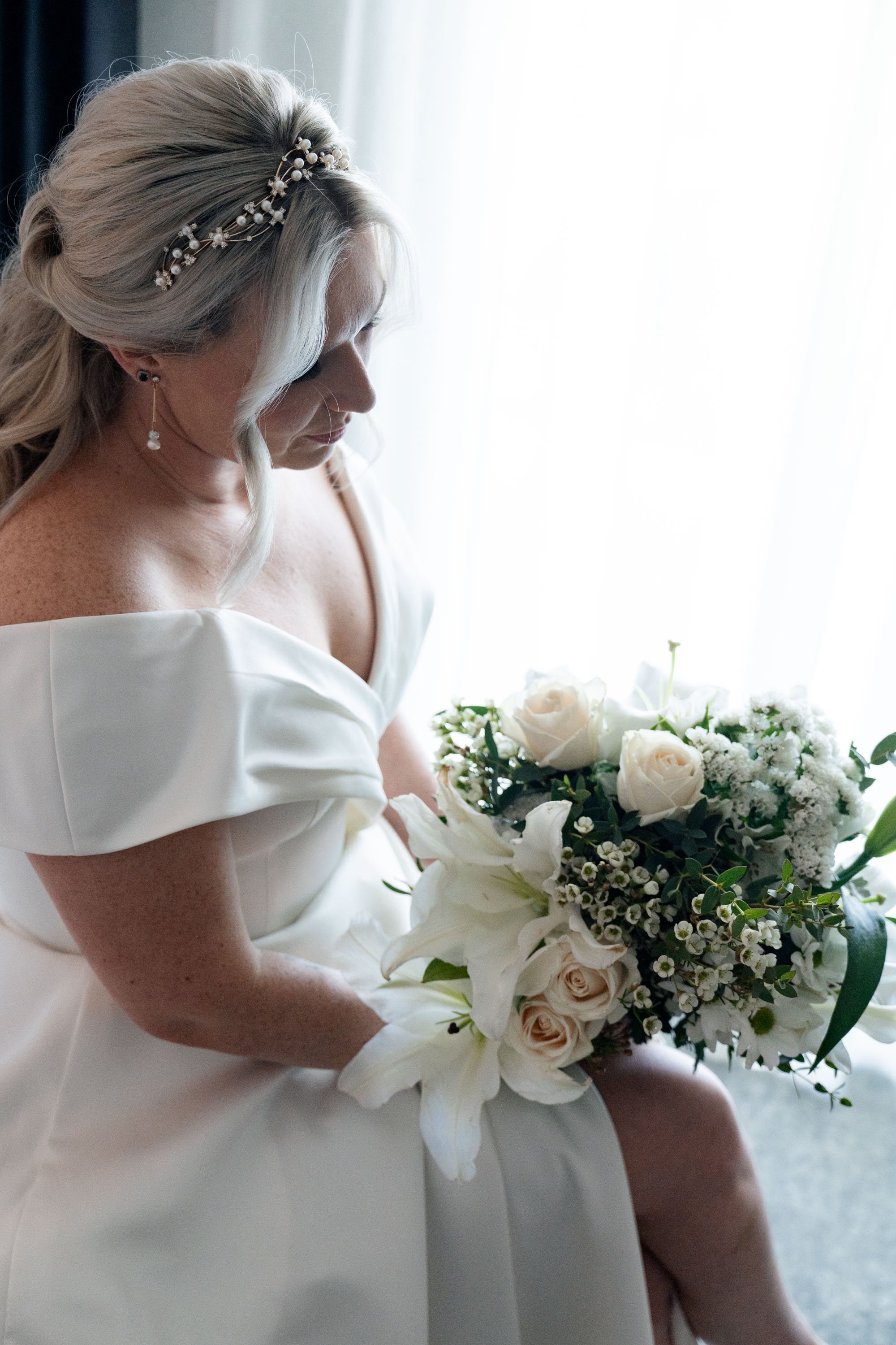 Kyra, the bride, looking down at her bouquet while sitting, reflecting quietly and enjoying a peaceful moment before the wedding festivities