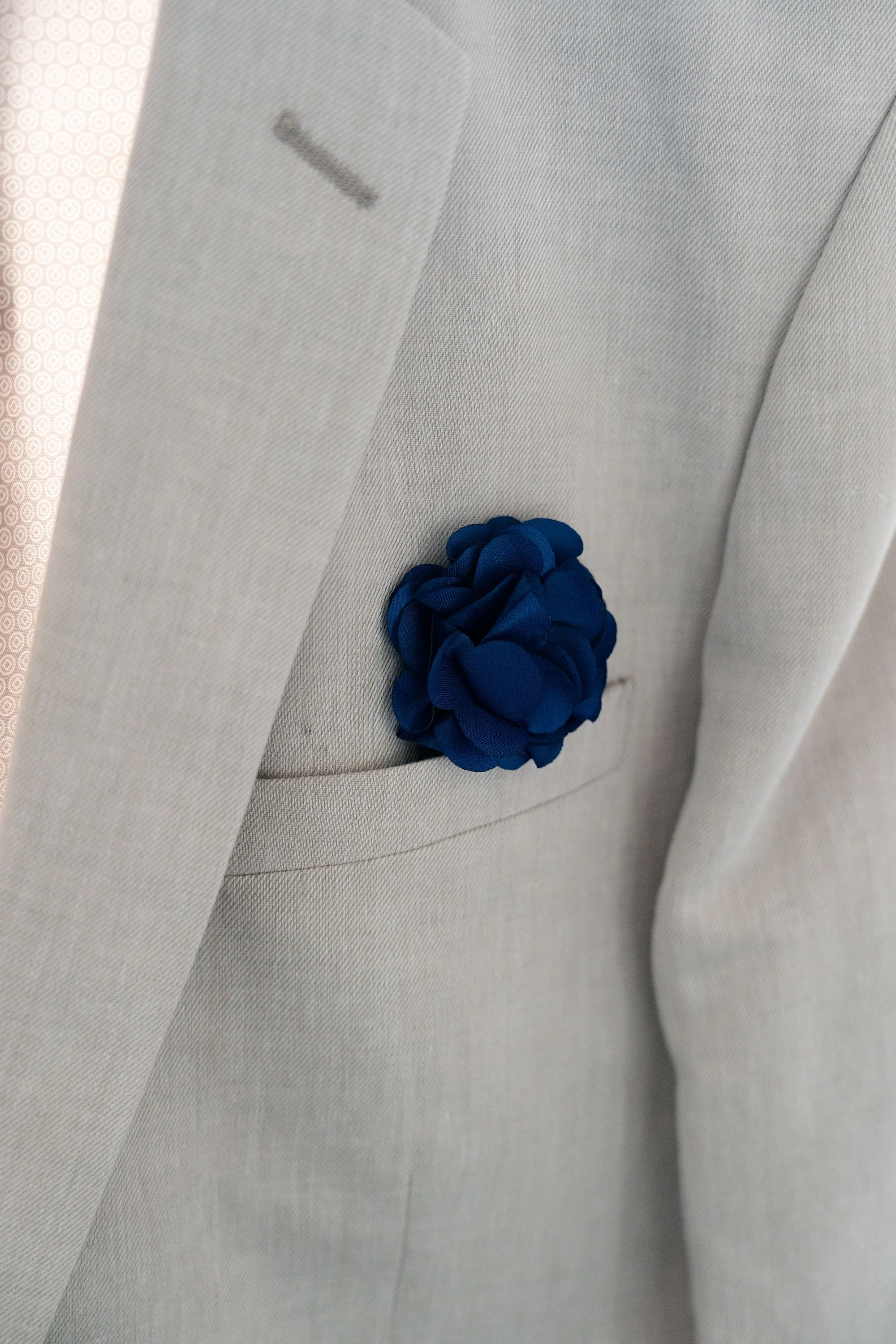 Blue pocket square flower on Thomas's jacket, adding a touch of elegance and color to his wedding attire