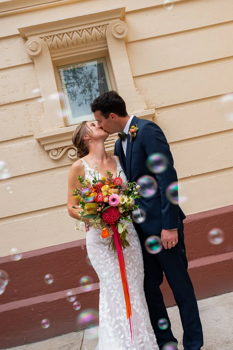 bride and groom kissing out side church with bubble flying in front them