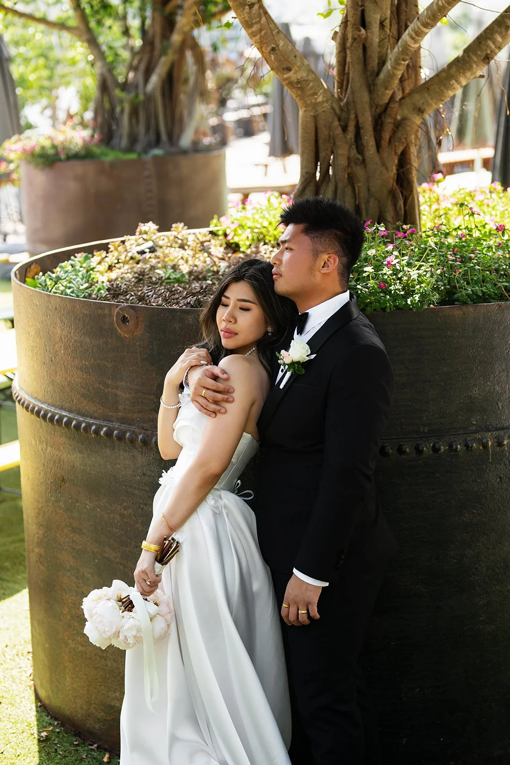 Groom Kai holding the bride Tiffy’s shoulder from behind as she gently rests her head on his chest, holding his arm with her eyes closed. The intimate moment reflects deep connection and tenderness, showcasing their love and tranquility in this roman