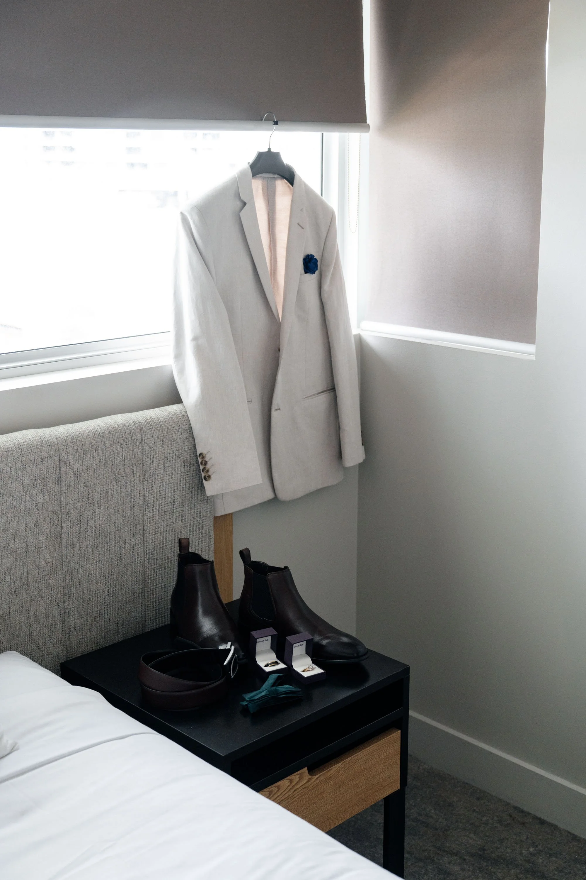 Groom Thomas's jacket, shoes, and wedding rings neatly placed on a table, capturing the details of his attire before the wedding ceremony
