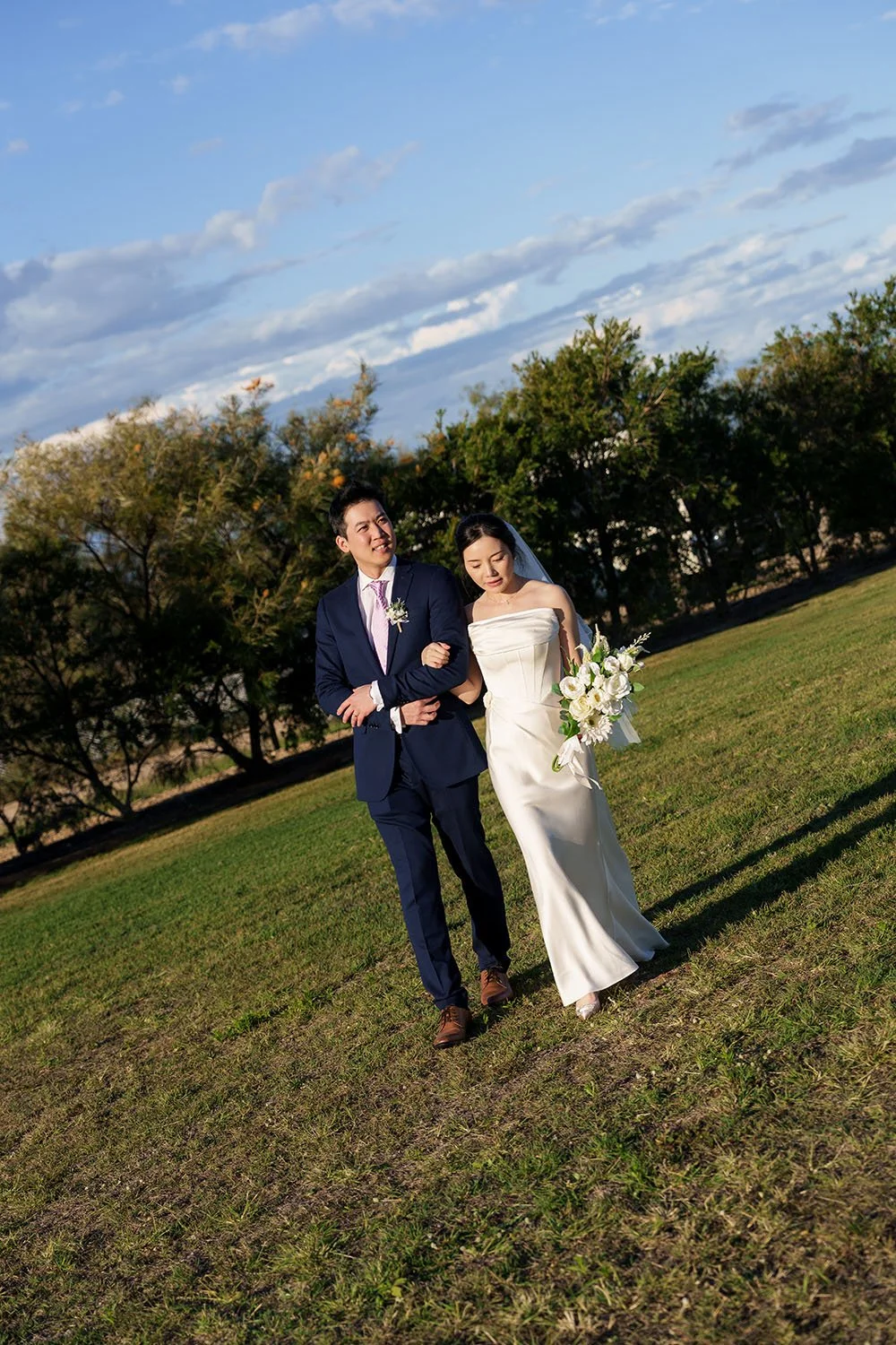 Bride Flora walking arm-in-arm with groom Eric looking into the distance along a scenic lawn path