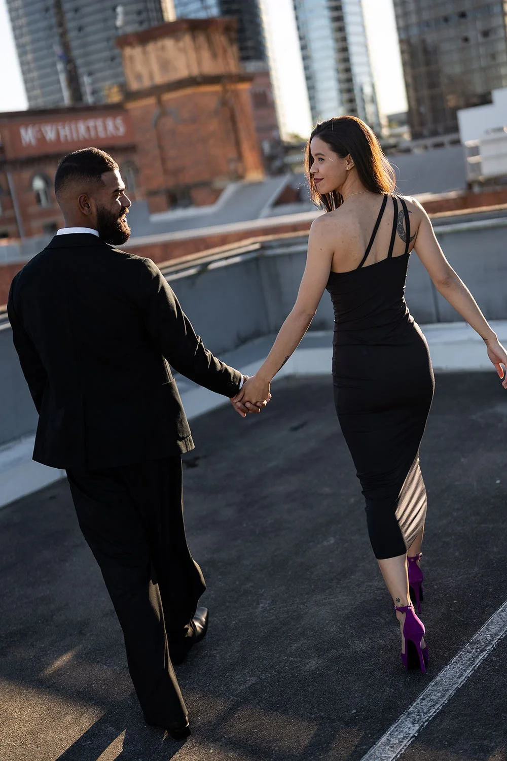 Jasmin and Jay holding hands look at each while walking away from the camera with laughing