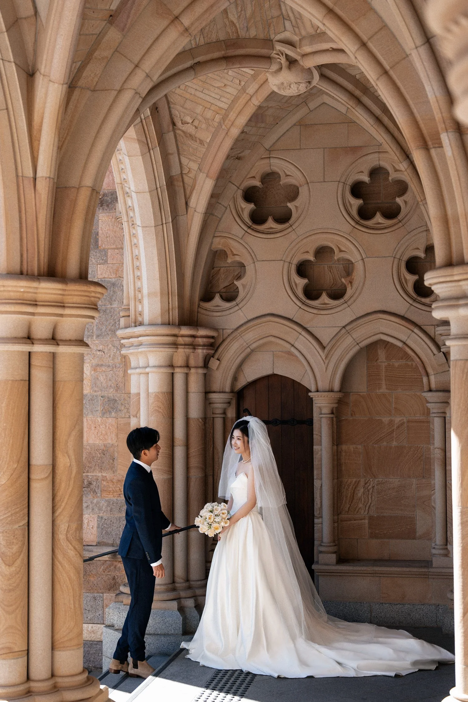 groom Leo standing on the stairs and bride Cassie look at him outside St John's Cathedral in Brisbane
