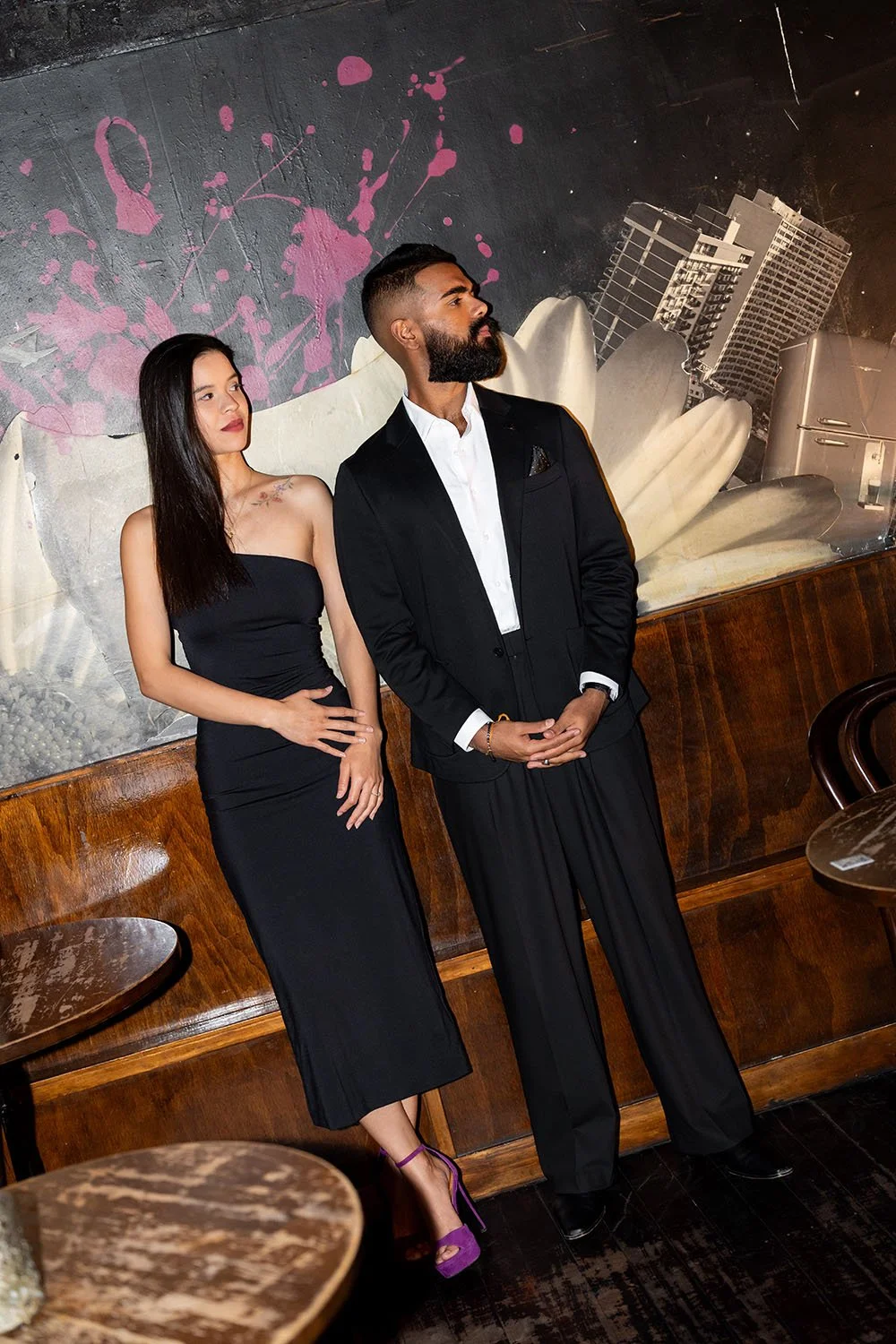 Jasmin and Jay stand side by side look away from the camera