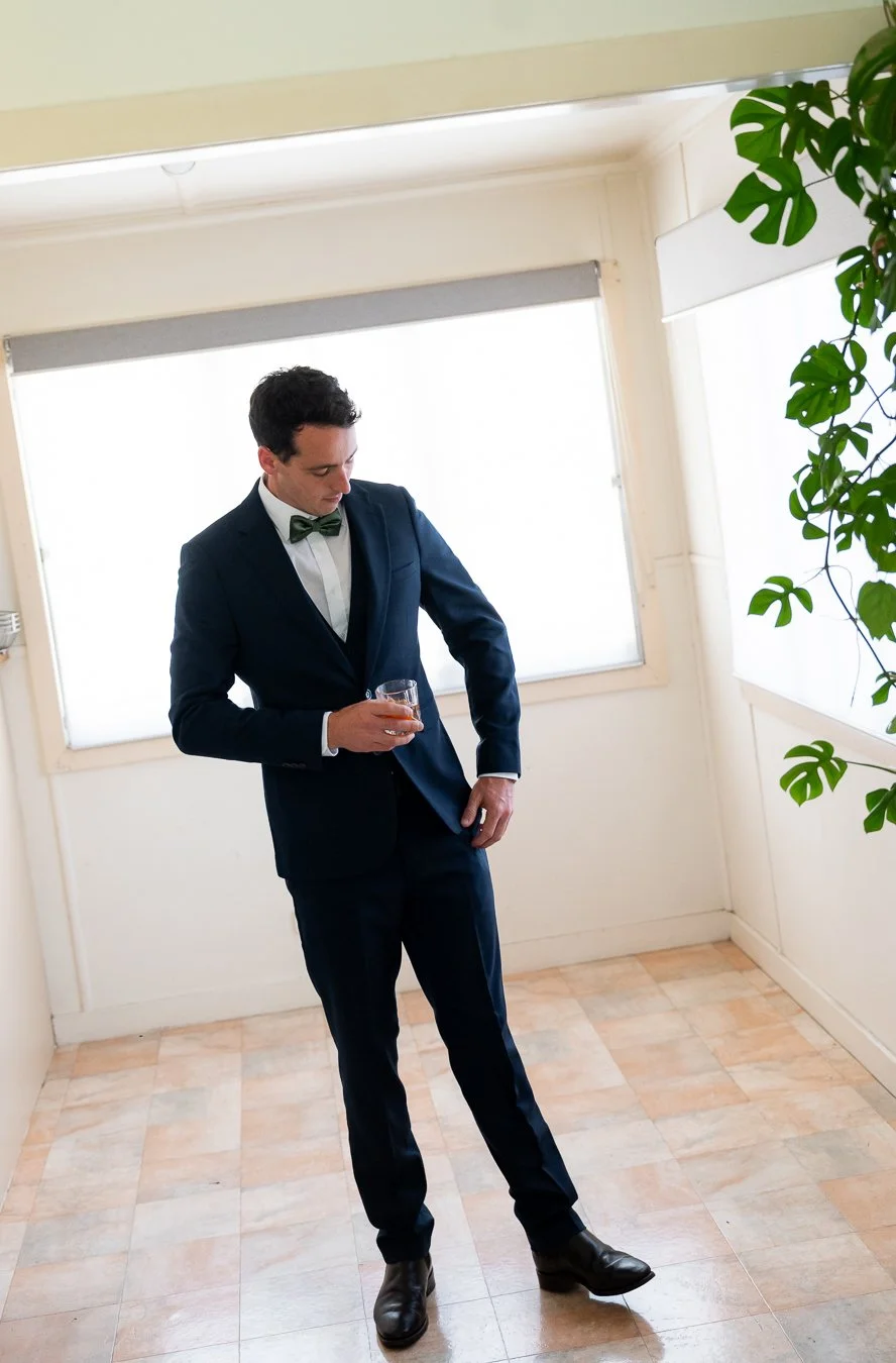 The groom, dressed in his suit, held a glass and looked down at the ground