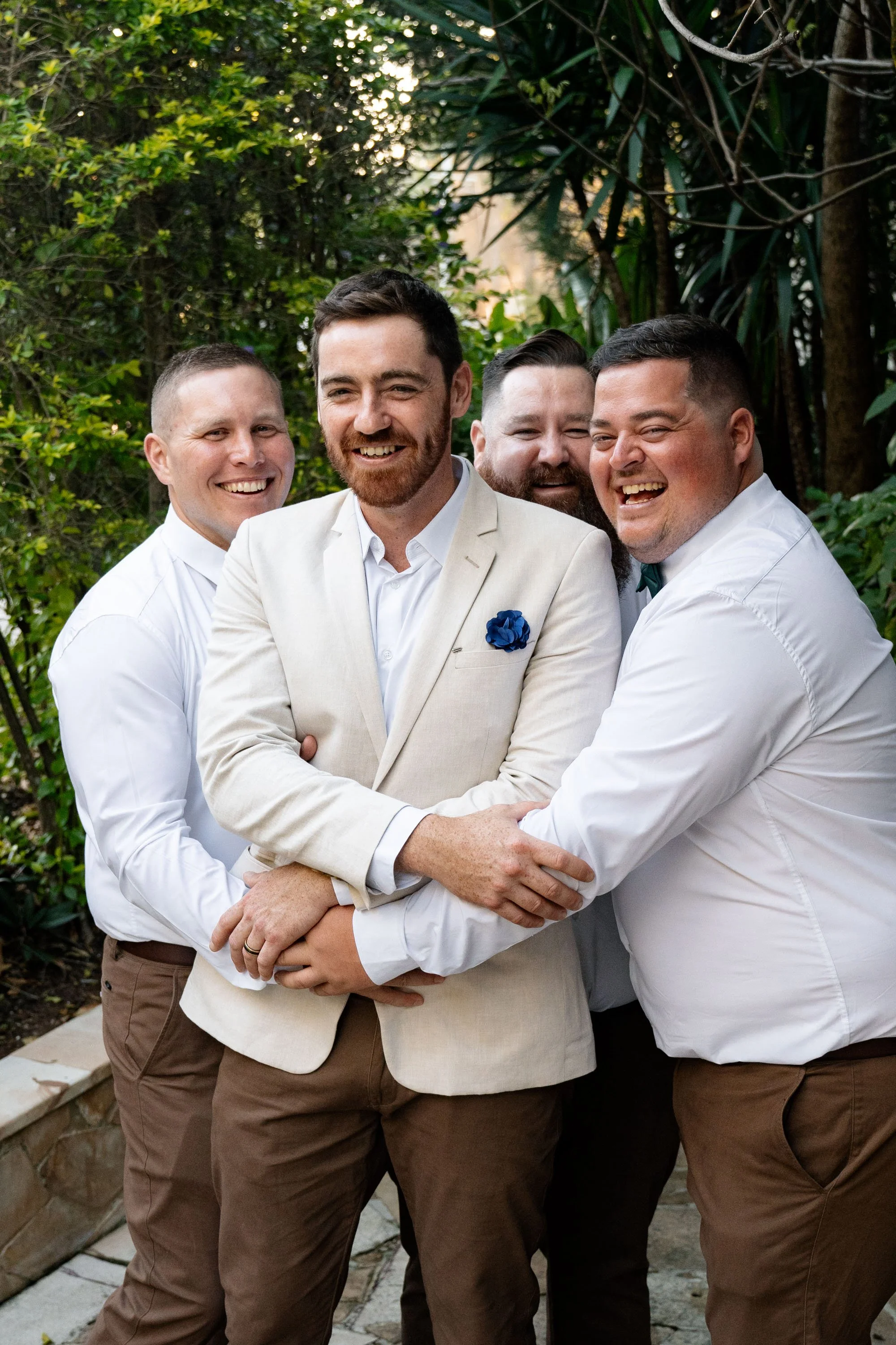 Thomas's groomsmen playfully holding him, as they all look toward the Brisbane wedding photographer, Whistler, capturing a fun and lighthearted moment