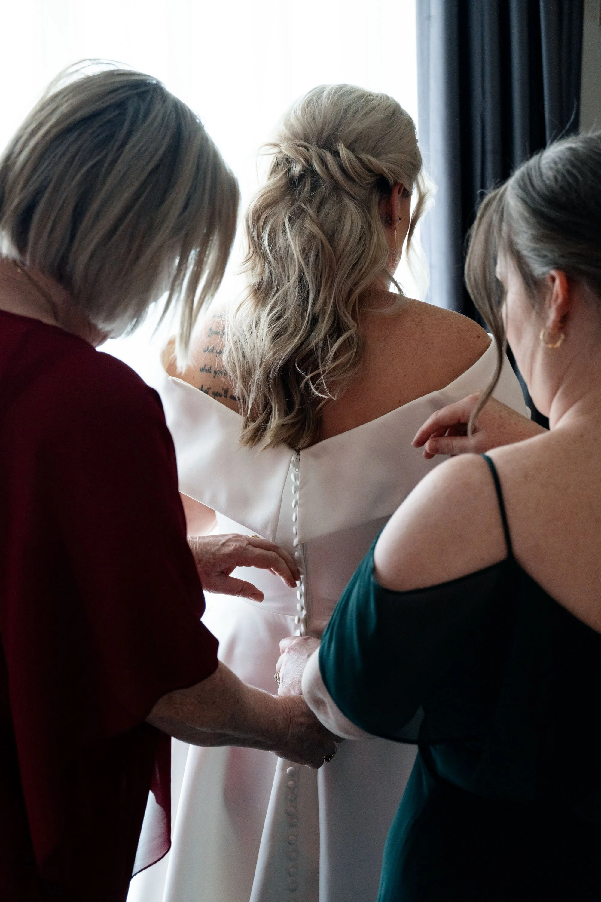 Bride's mum and sister standing behind her, offering support and love as they share in the emotional moments before the wedding ceremony.