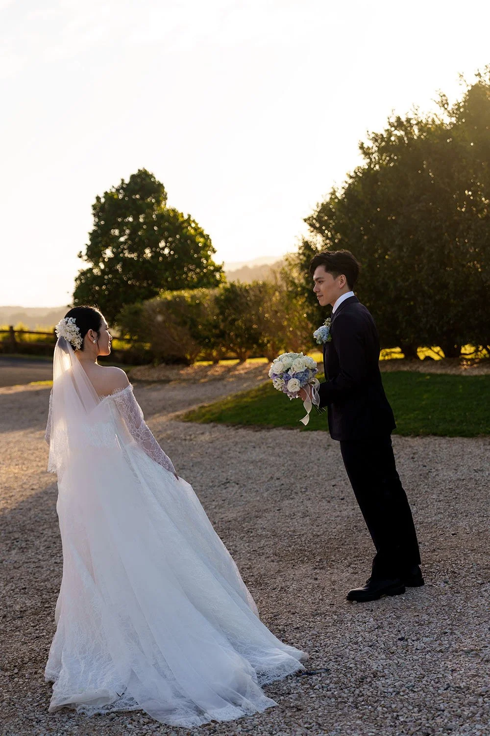 Michael holding a flower stand, Lisa holding her wedding dress stand two steps away from him and they both look at each other