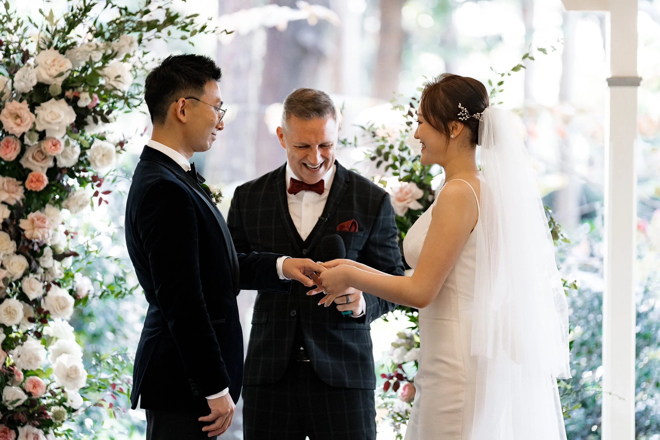 Bride smiling at groom Brus as she lovingly places the wedding ring on his finger. The intimate moment reflects their deep connection and the joy of exchanging vows, capturing the emotion and significance of this special part of their wedding day