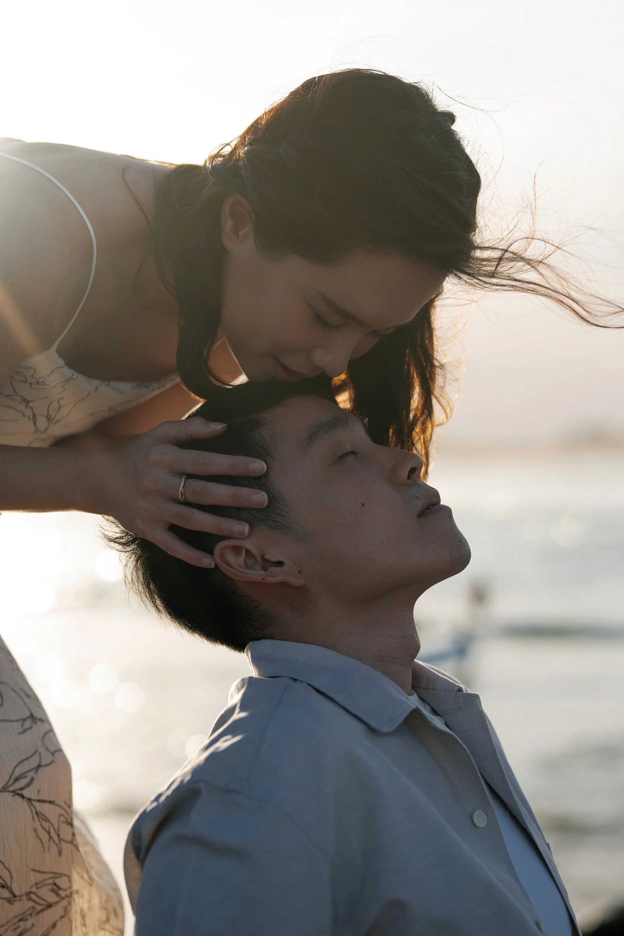 Krystel gently holding Paul's head as she leans in to kiss his forehead at Currumbin Rock. The intimate moment, captured against the rugged natural backdrop, reflects their deep affection and the peaceful beauty of their surroundings.