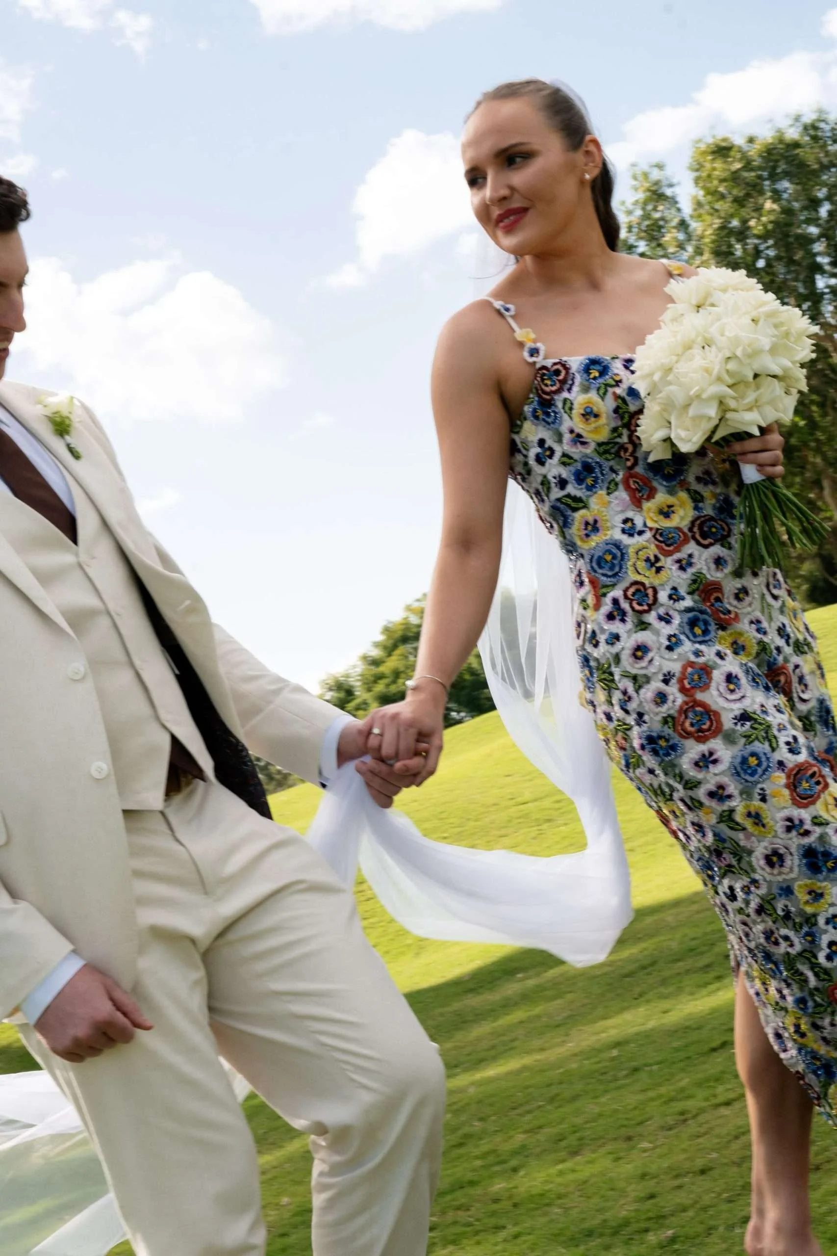 Bride and groom walking hand in hand on the grass with a softly blurred background.