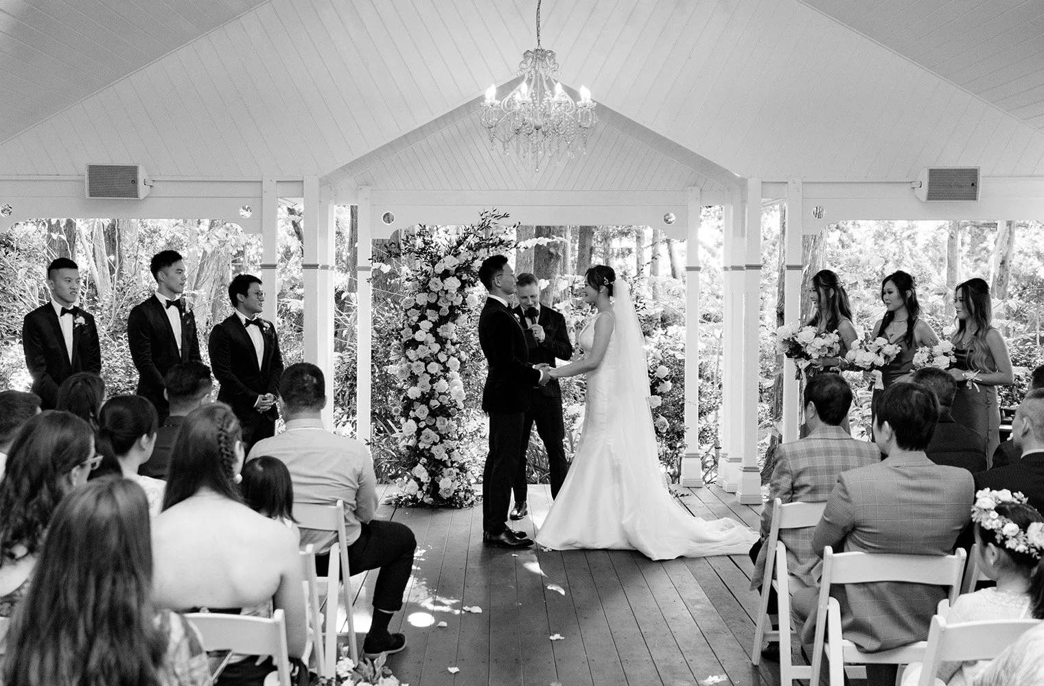 bride and groom holding hands look at each other in ceremony standing with all bridal party